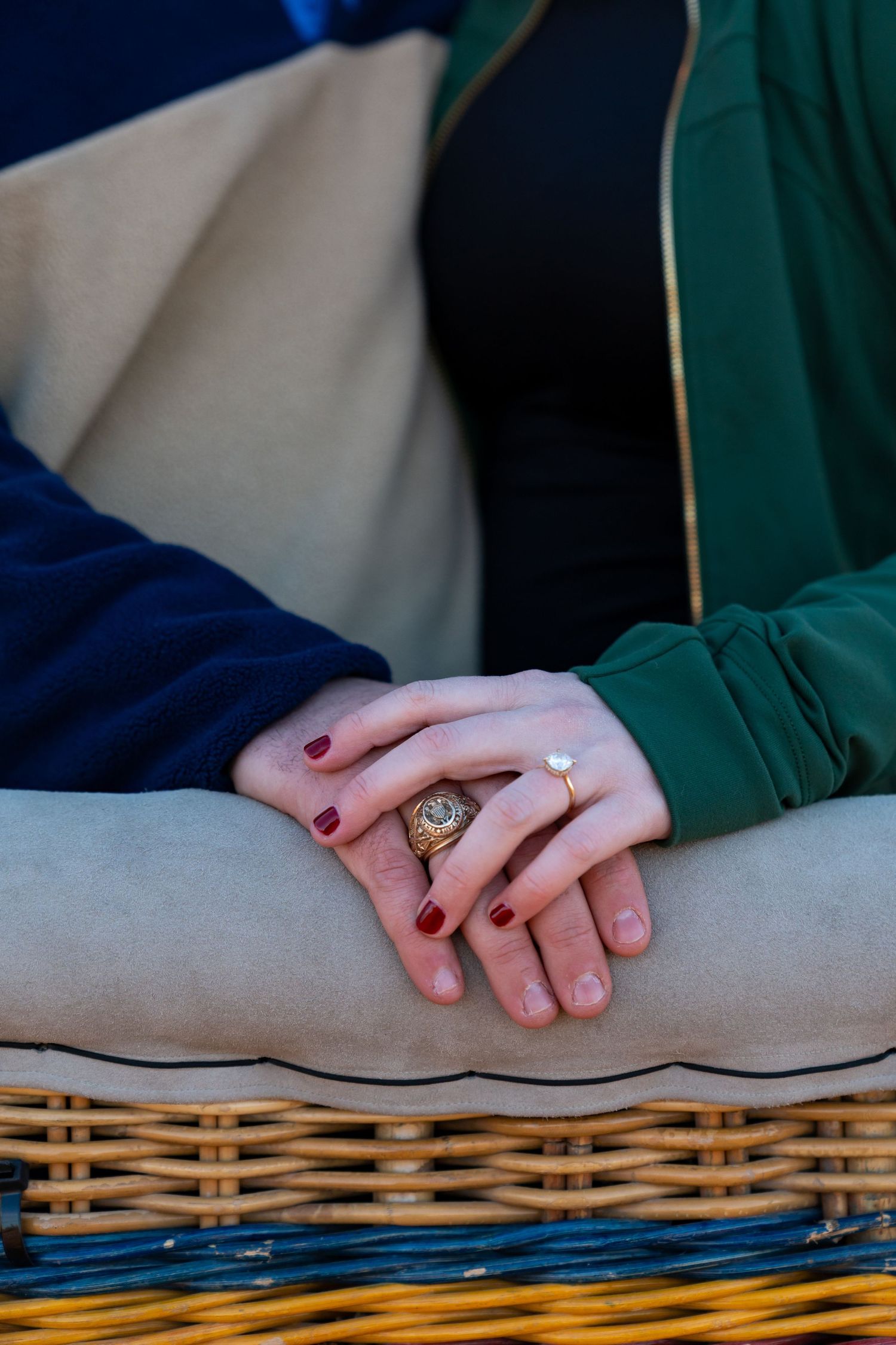 Close-up of couple's hands with engagement ring resting on woven blanket with colorful stripes.