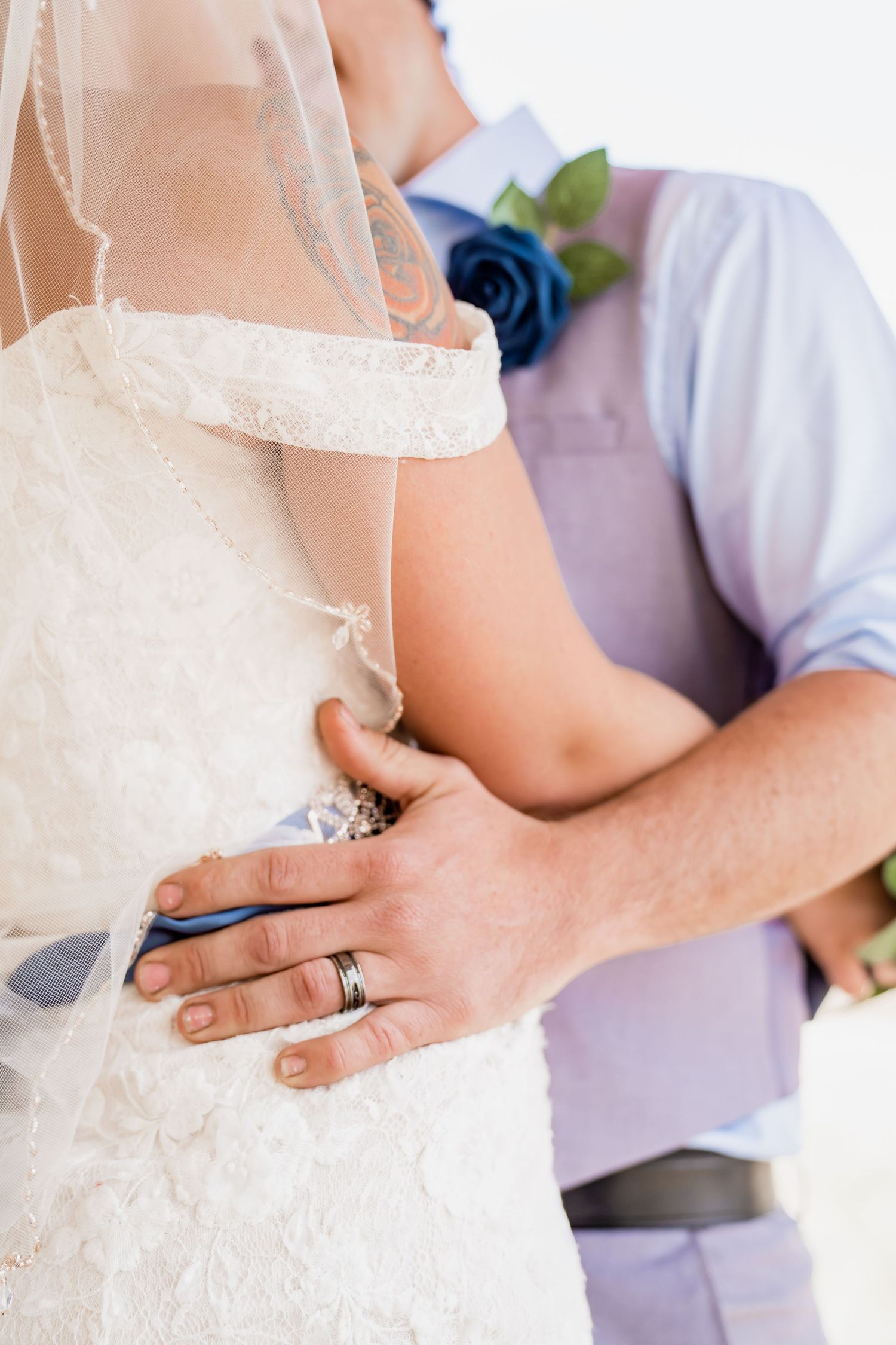 Close-up detail of hands wearing wedding rings against a white lace dress.