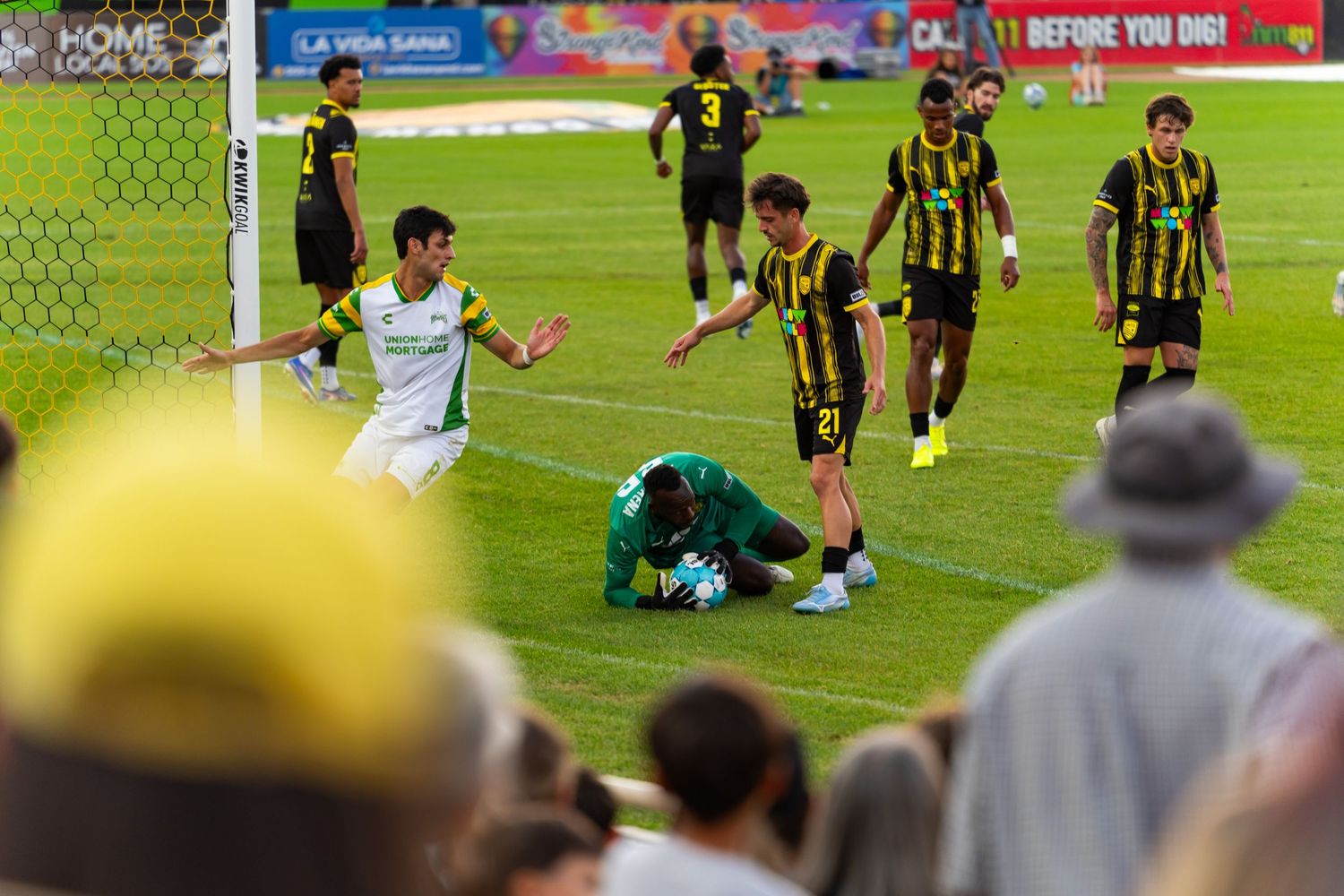 Soccer players react during a match, with a goalkeeper kneeling on the field while teammates in yellow and black look on.