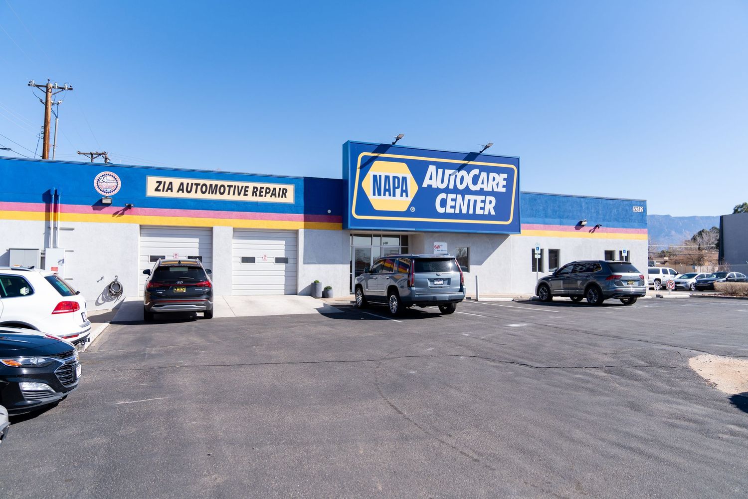 A strip mall parking lot with several parked cars and commercial storefronts visible in a suburban setting.