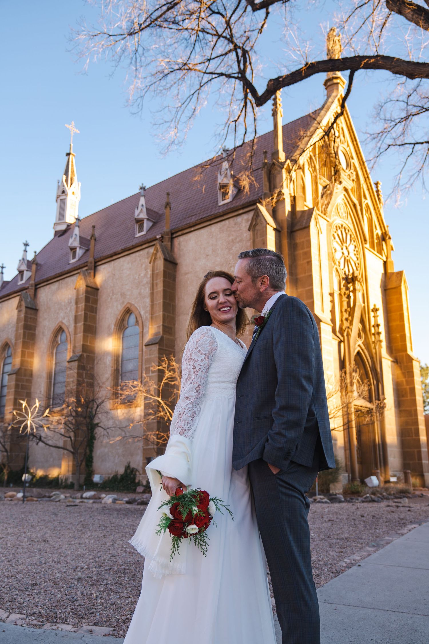 Wedding couple poses in front of a historic sandstone church during golden hour.