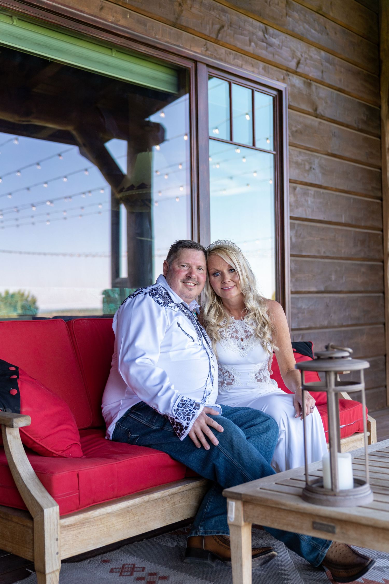 Couple relaxing together on a wooden porch bench with red cushions at a rustic cabin.