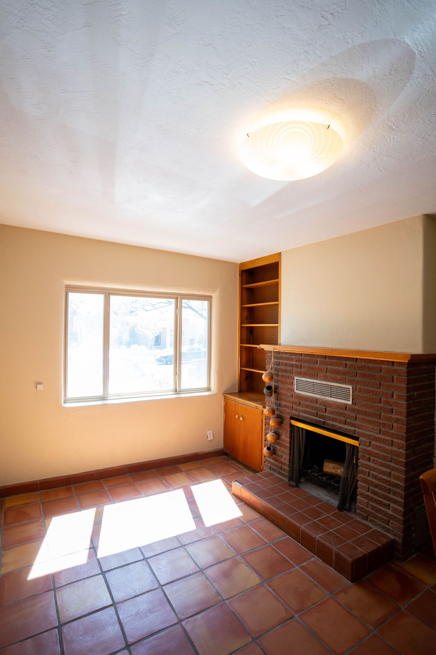 Empty room with terracotta tile flooring, brown brick accent wall, and large windows letting in natural light.