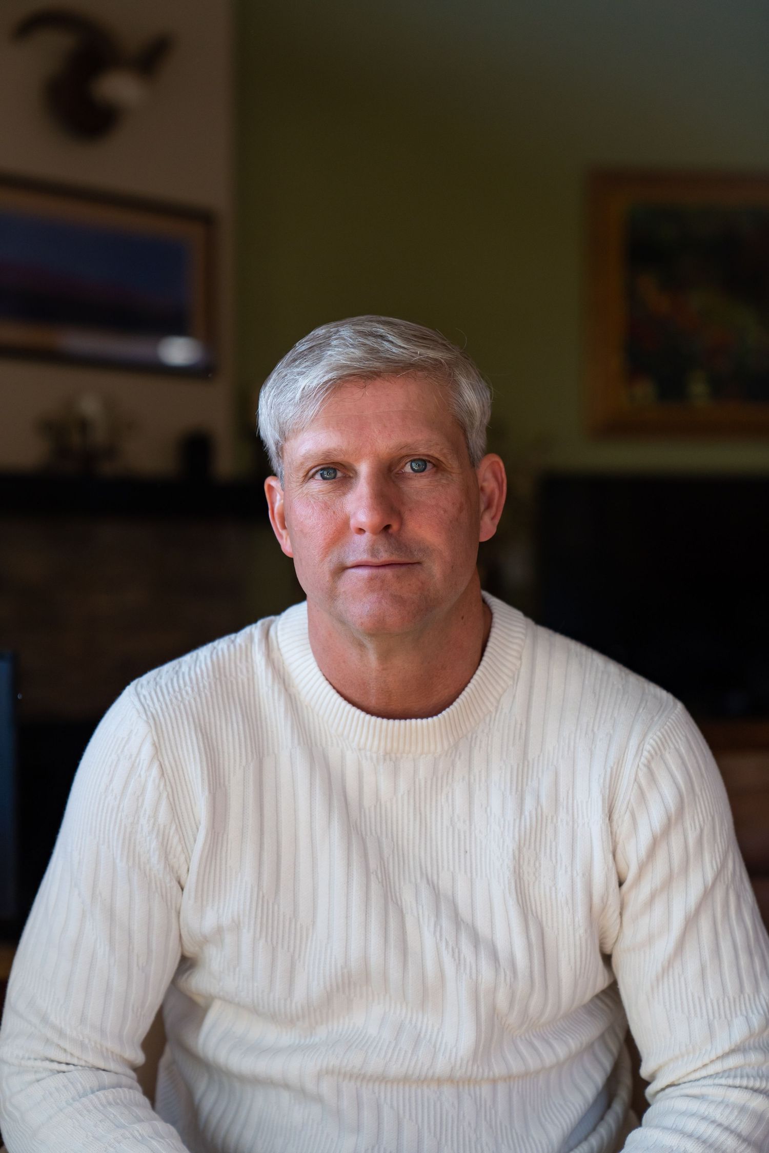 Indoor portrait of a person wearing a white ribbed sweater against a dark background.