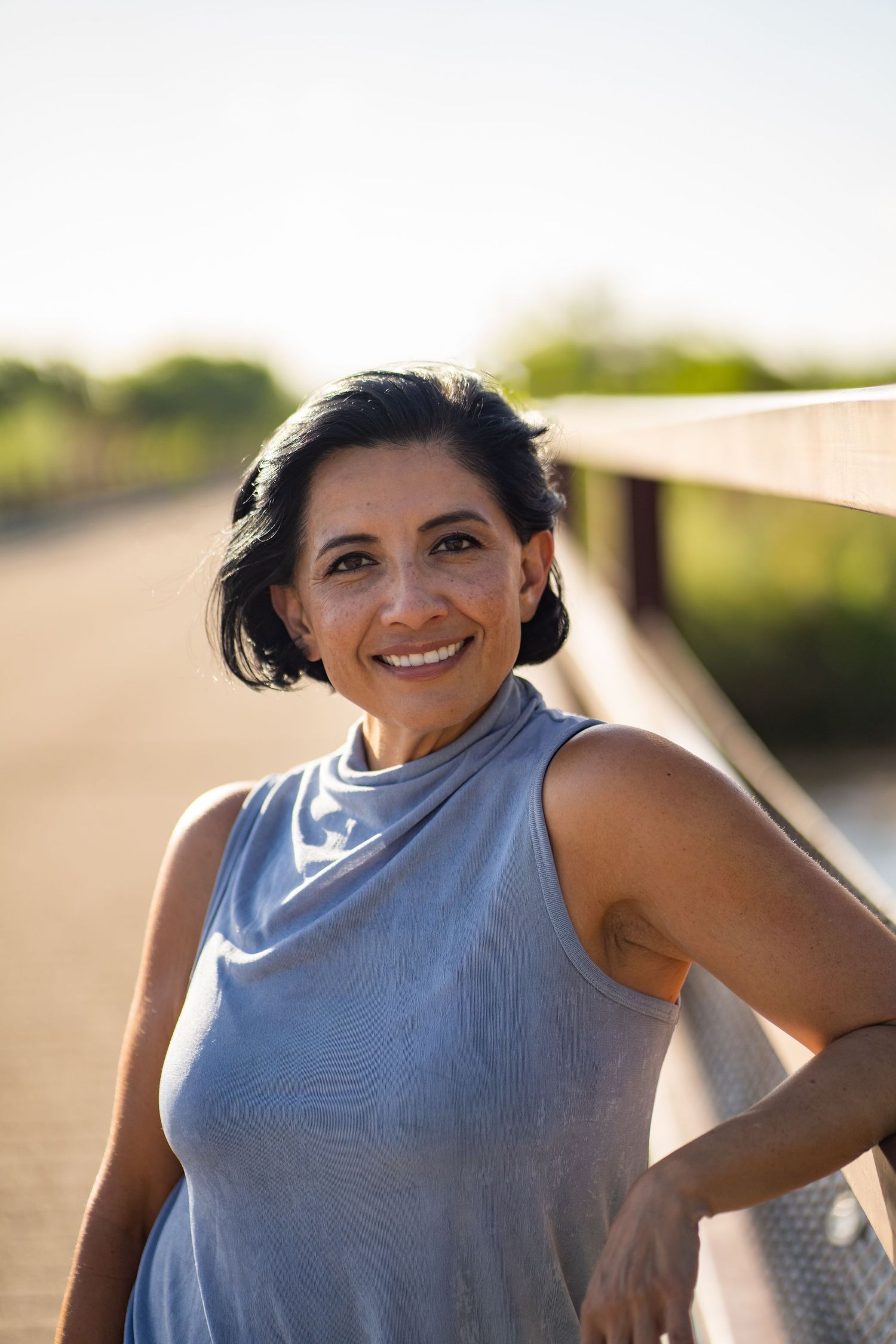 Person wearing sleeveless gray top poses in natural outdoor lighting.