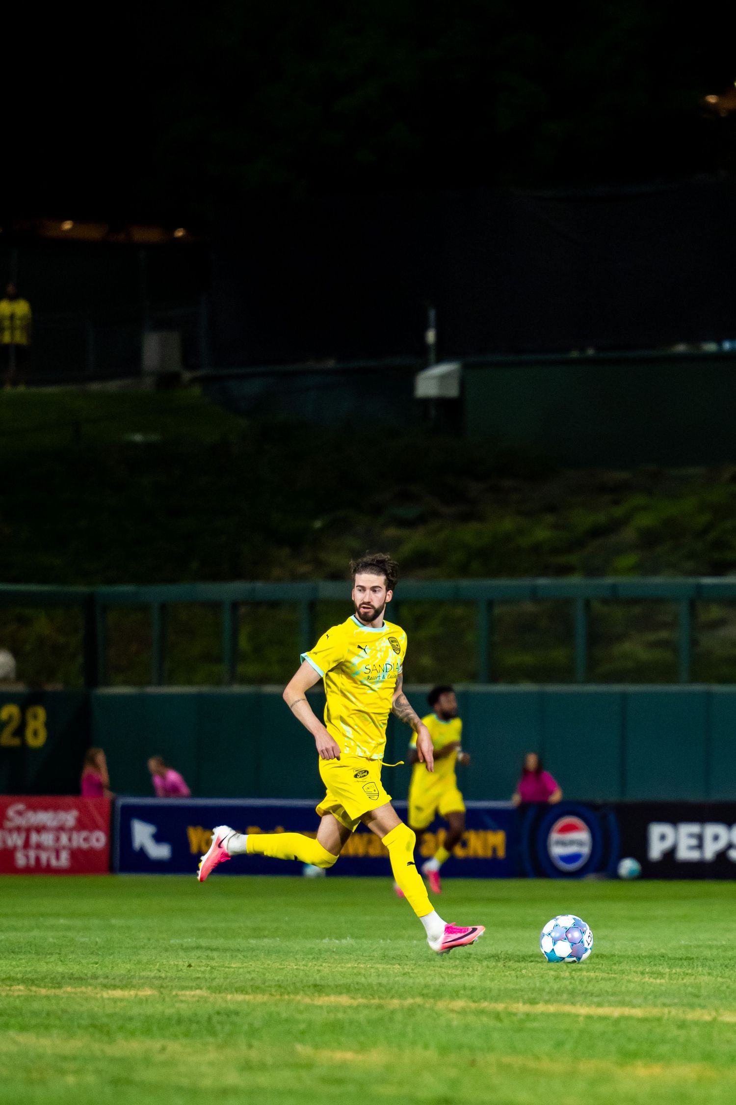Soccer player in yellow uniform dribbling ball on green field during a night match.
