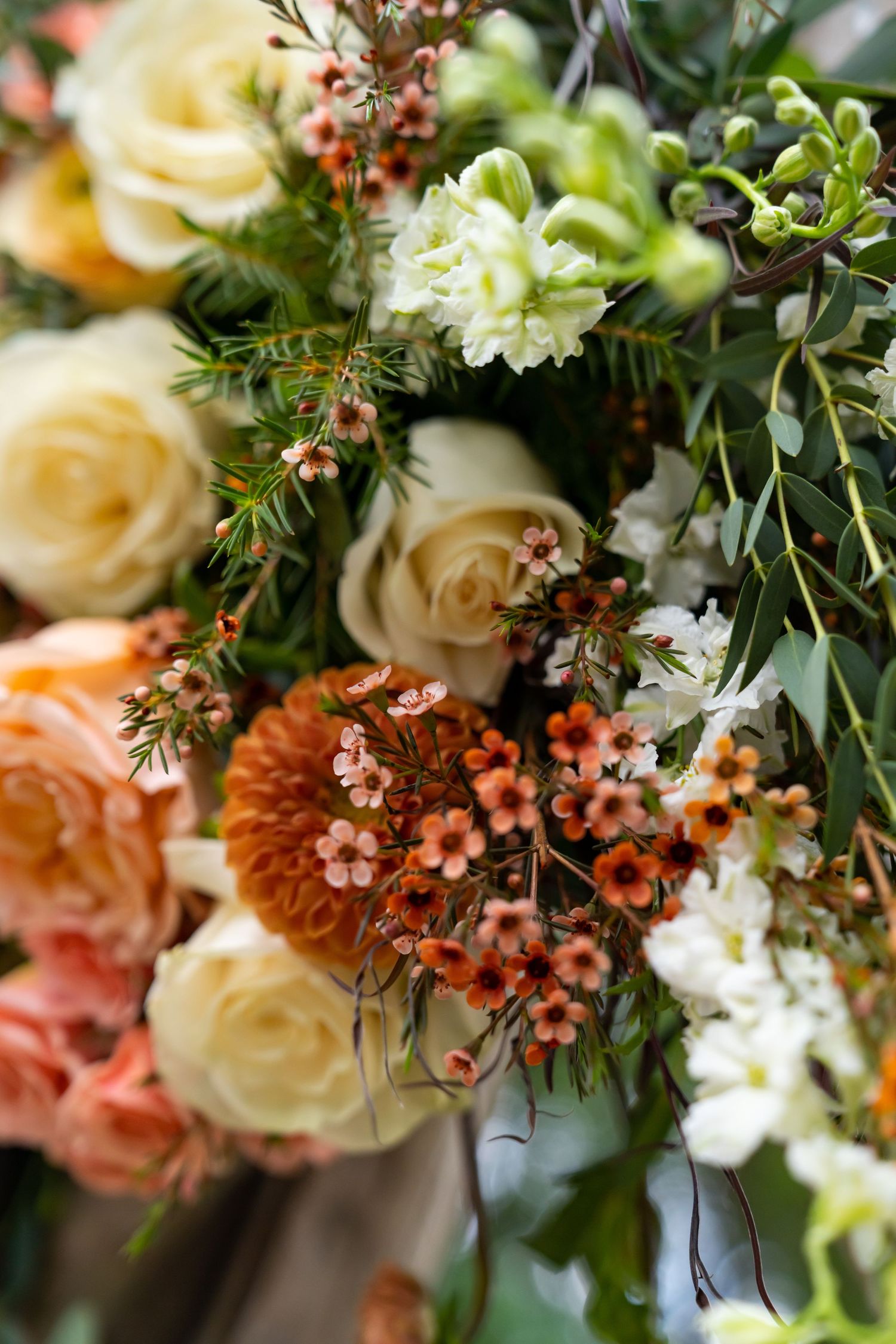 Close-up view of a romantic floral arrangement with cream roses, coral blooms, and delicate greenery in soft focus.