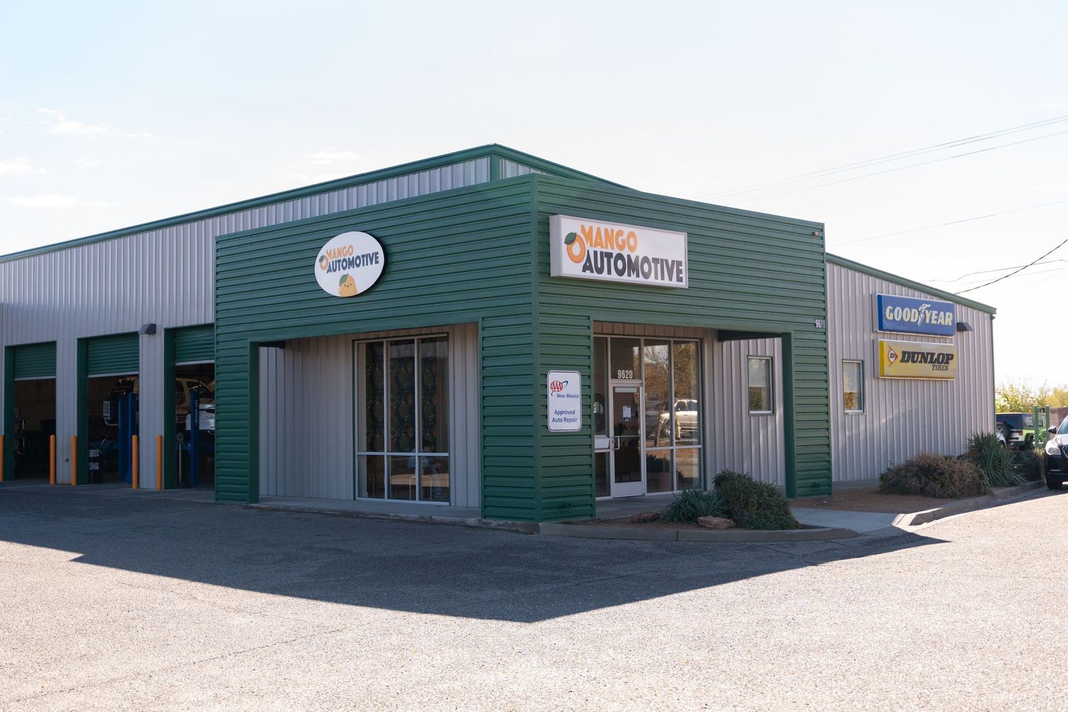 Exterior view of a green and gray commercial auto repair facility with multiple service bays.