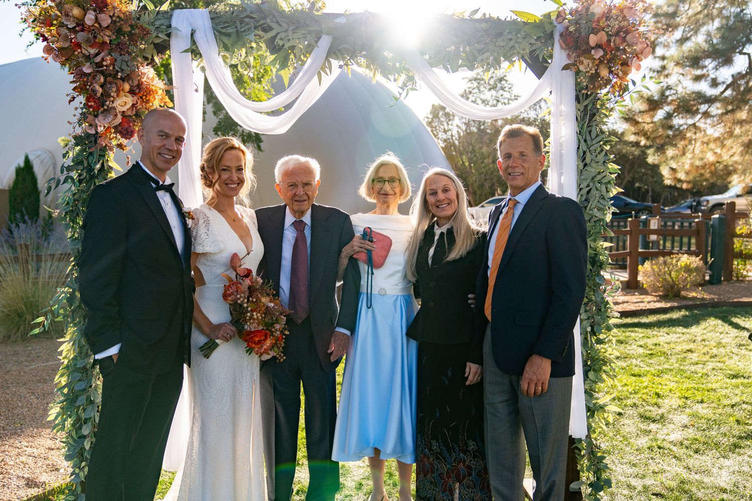 Family group poses for formal wedding photos in front of rustic backdrop.
