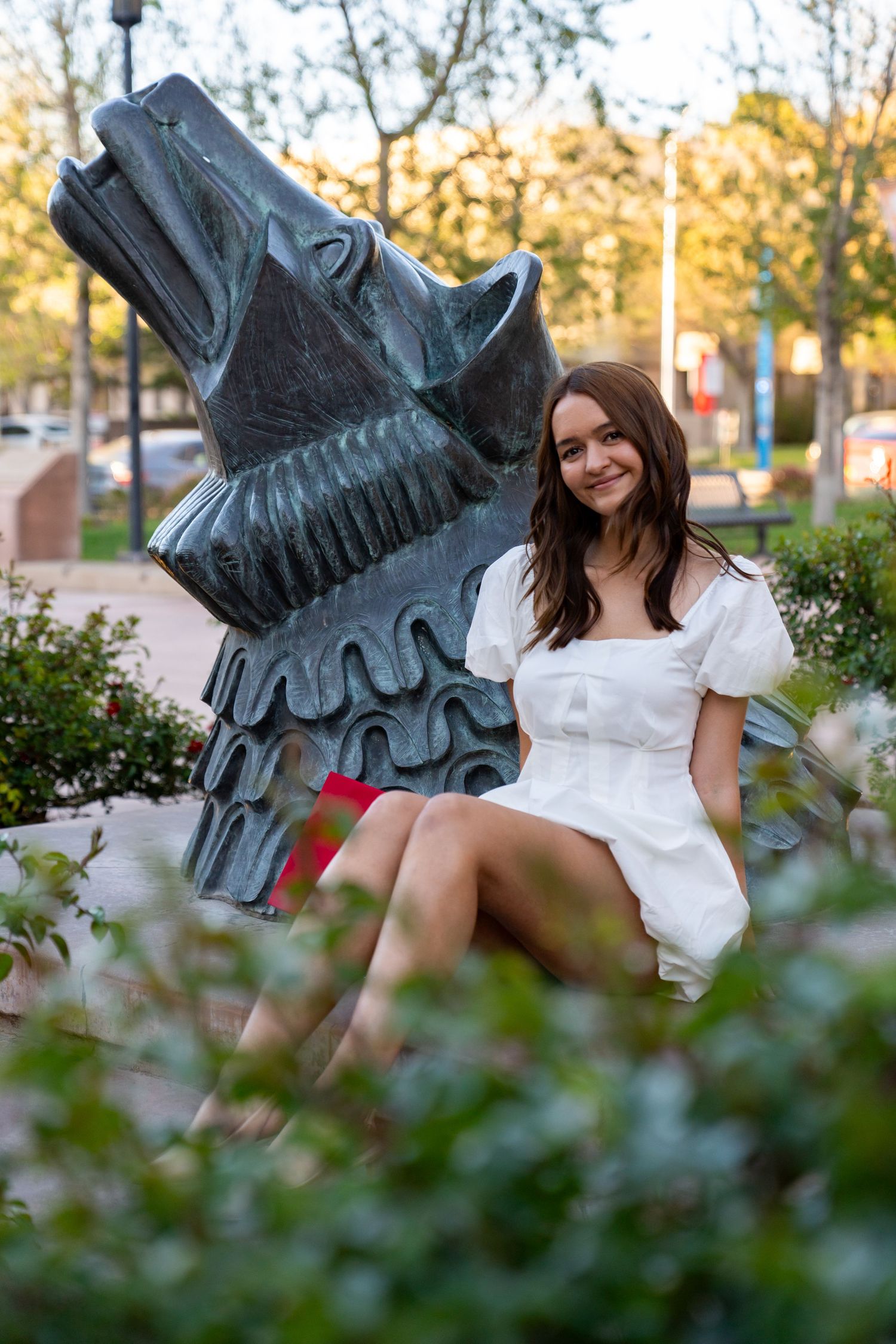 White summer dress against decorative metal sculpture in urban garden setting.
