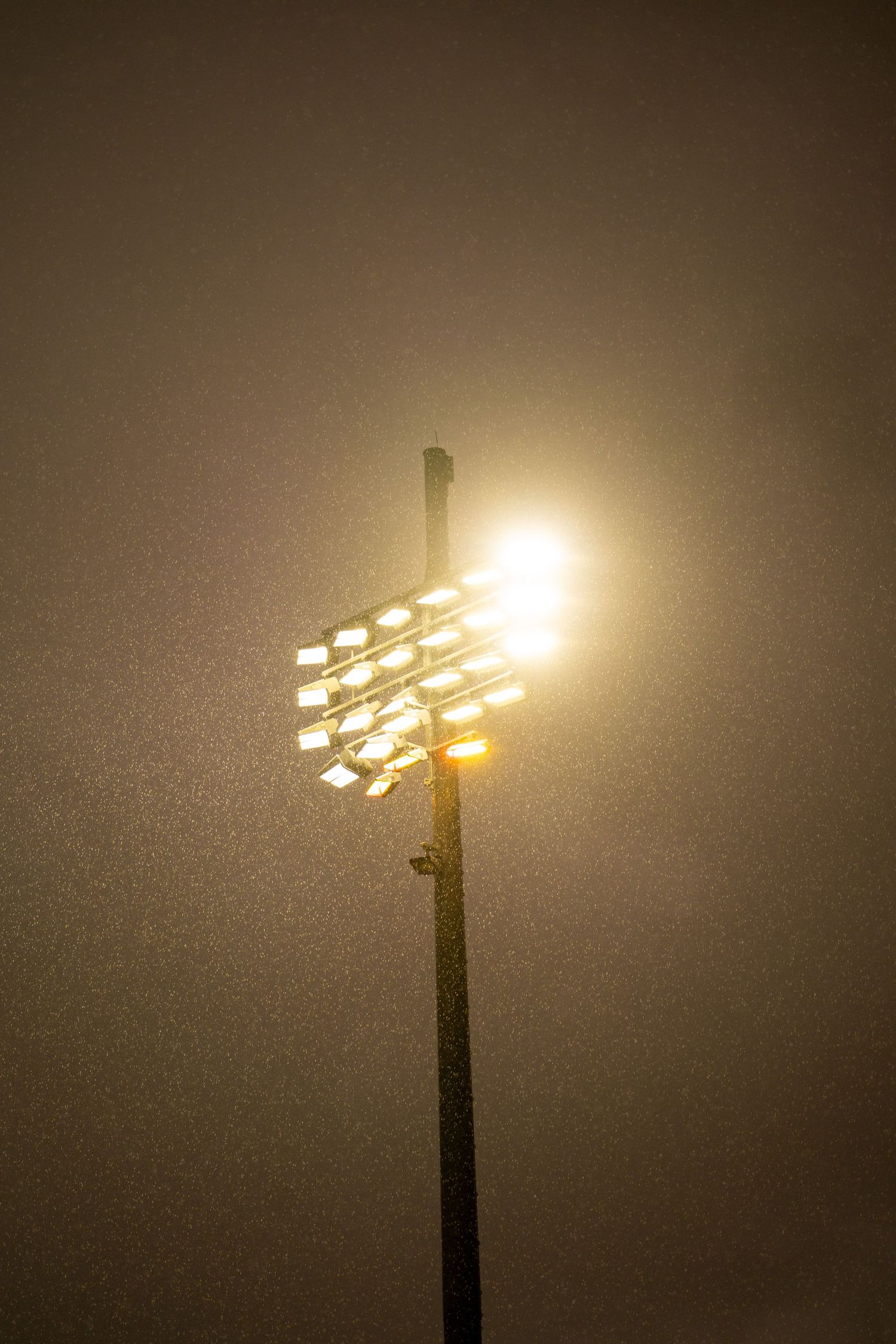 Stadium floodlight glowing brightly through foggy night sky, illuminating the field below.