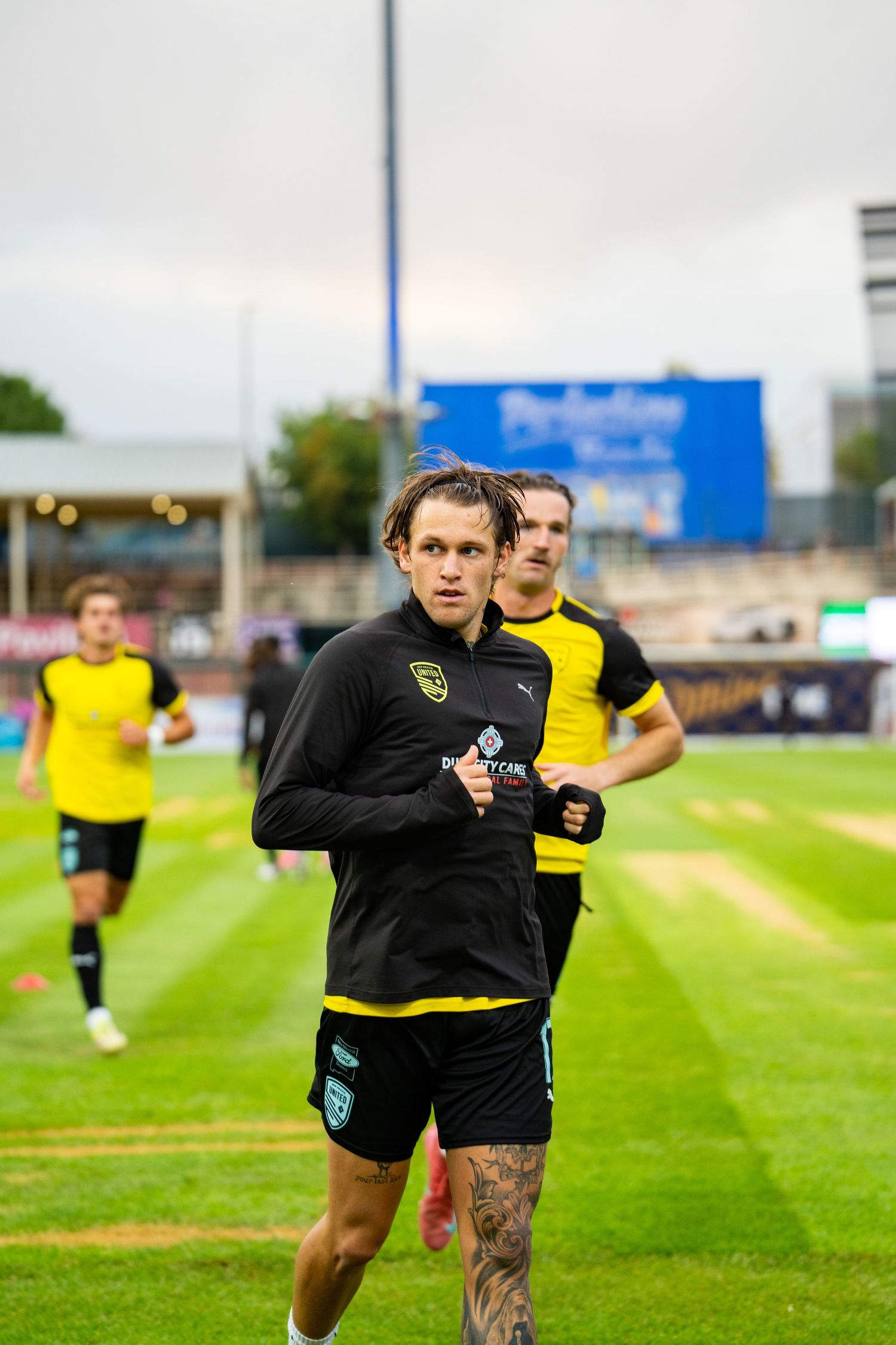 Football players in black and yellow kits warming up on a green pitch at a stadium before a match.