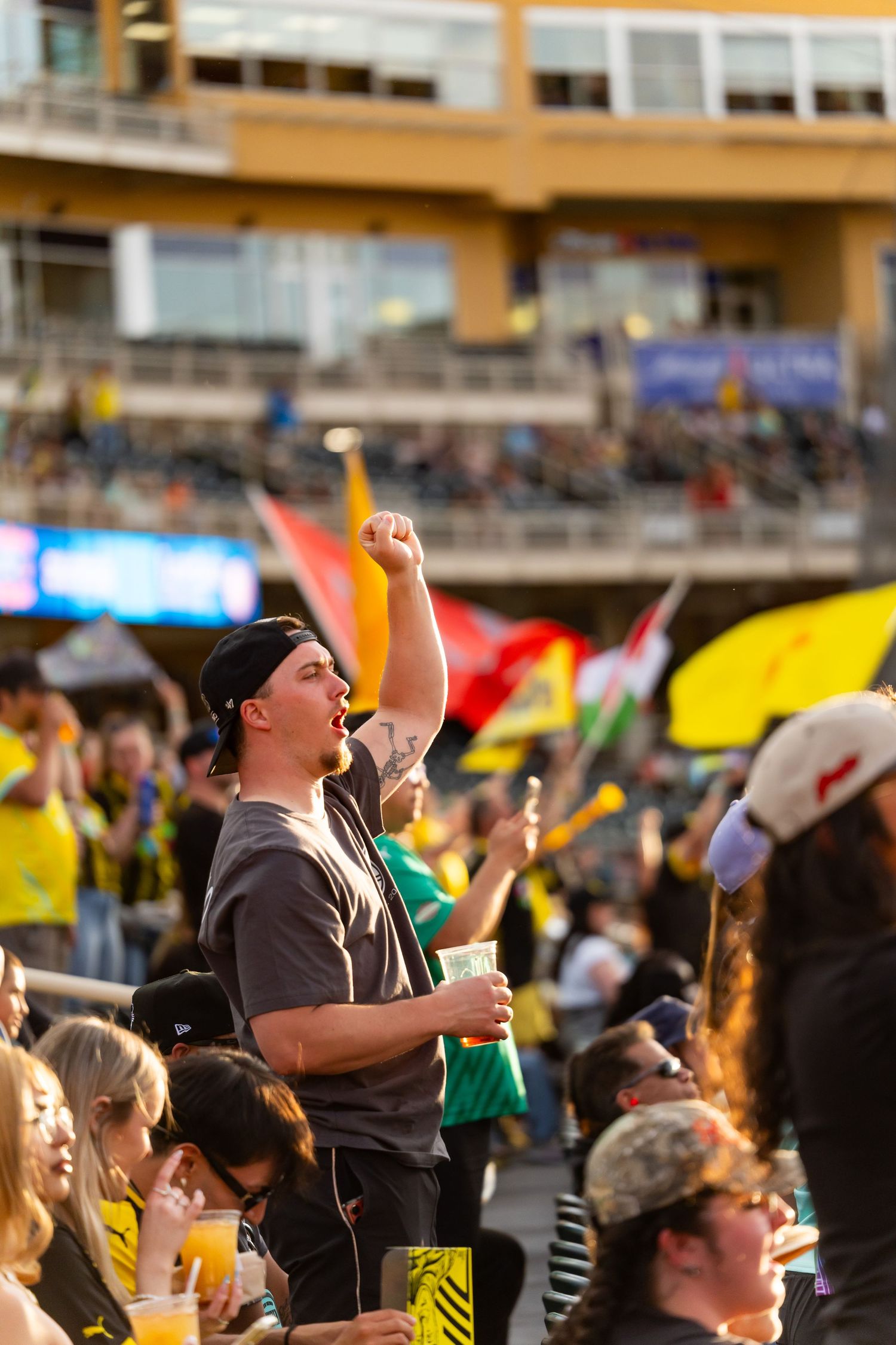Excited sports fan raises fist in celebration among crowd of yellow-clad supporters at outdoor stadium event.