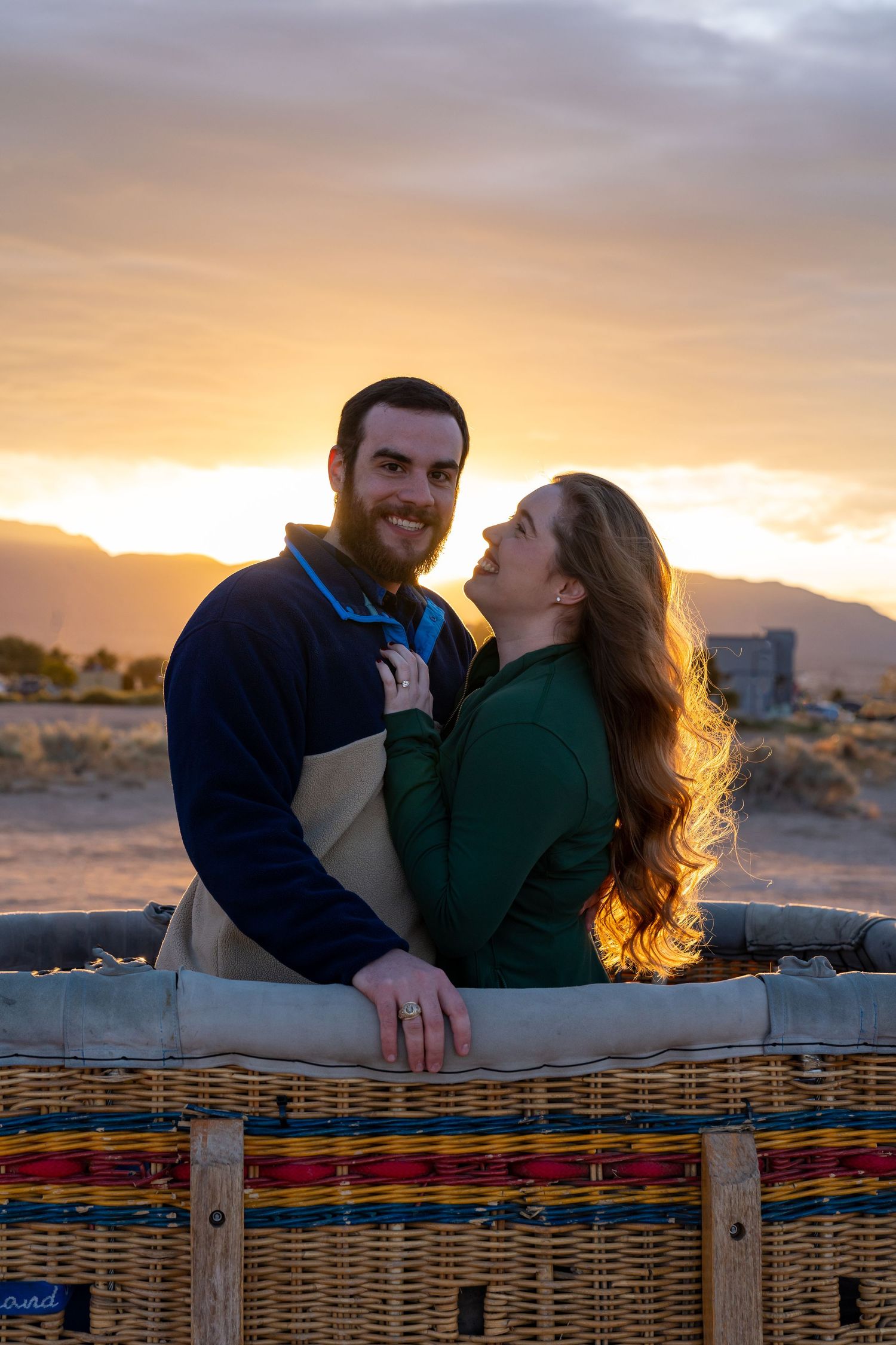 Couple shares romantic moment at sunset with colorful woven blanket in foreground.