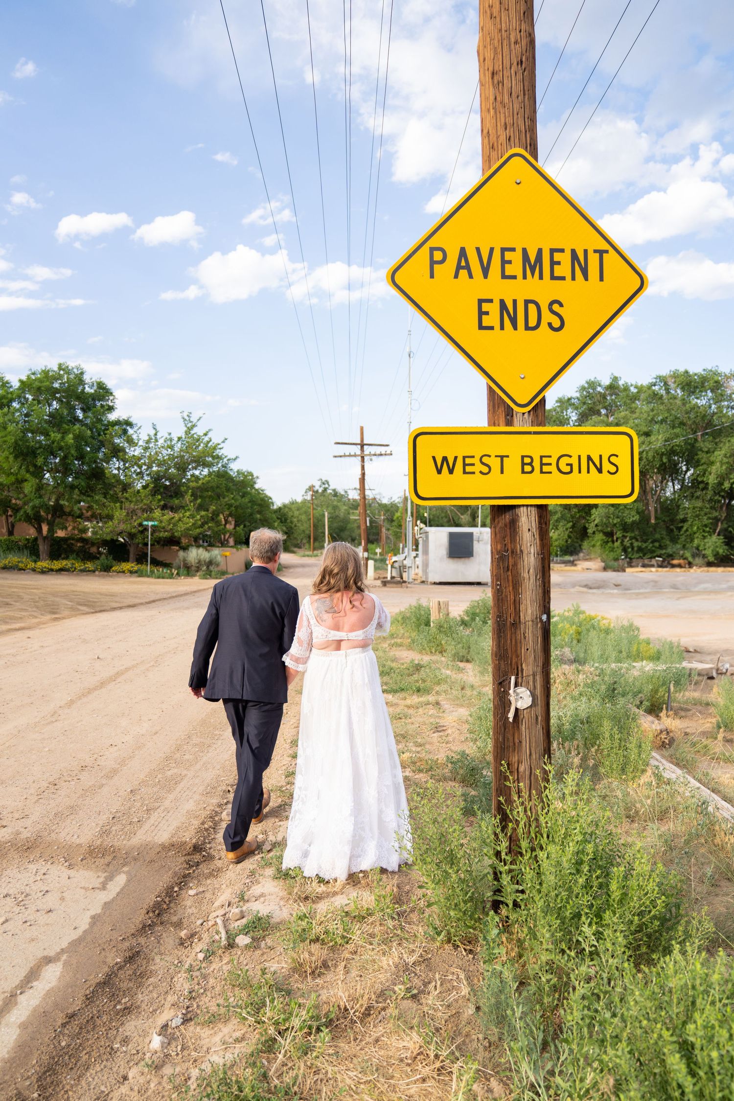 A couple walks down a dirt road past yellow road signs during a wedding photo session.
