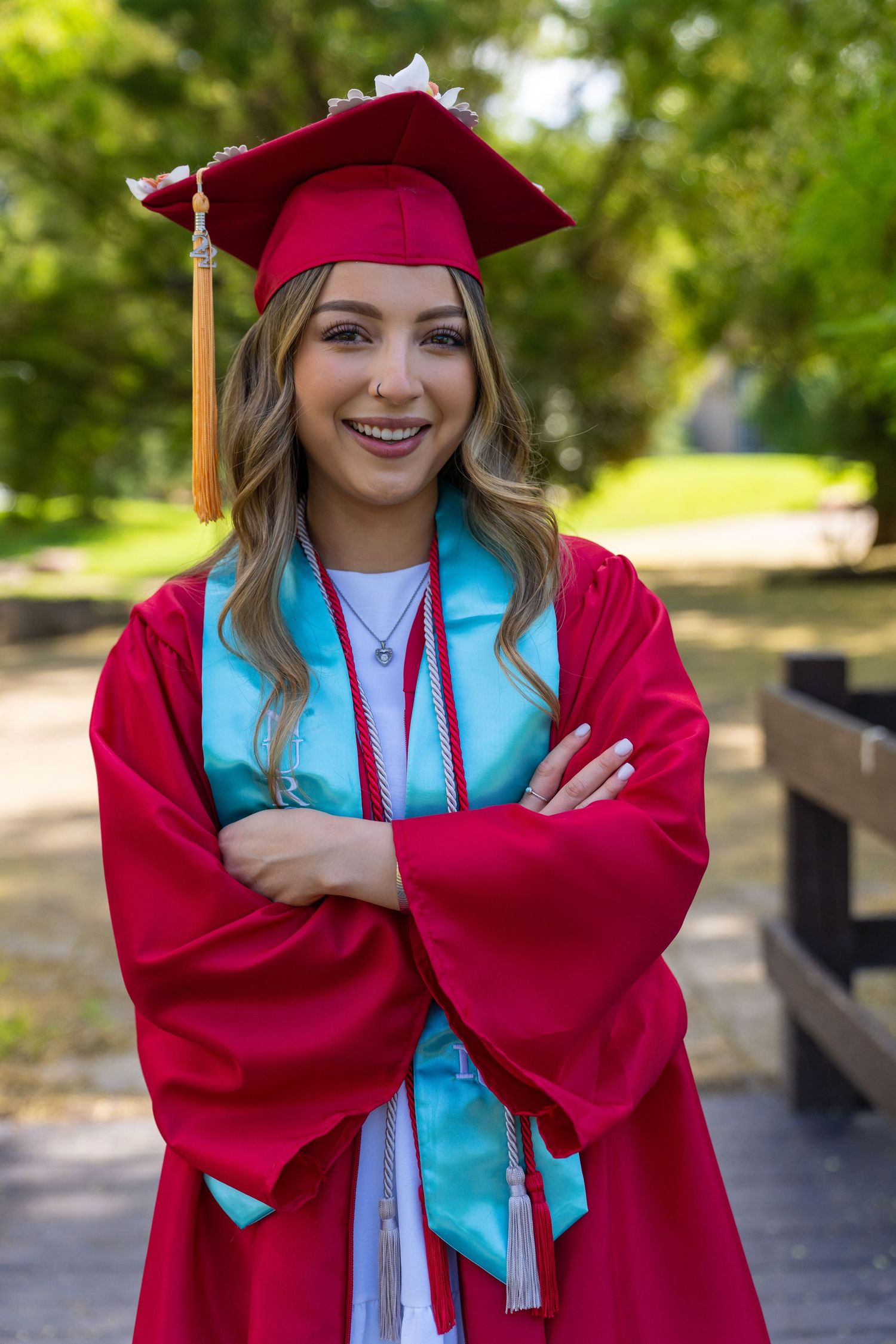Graduate in red cap and gown with gold tassel smiling outdoors on graduation day.
