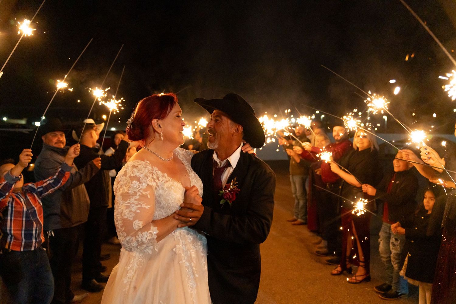 Newlyweds share a joyful moment during their sparkler exit at night.