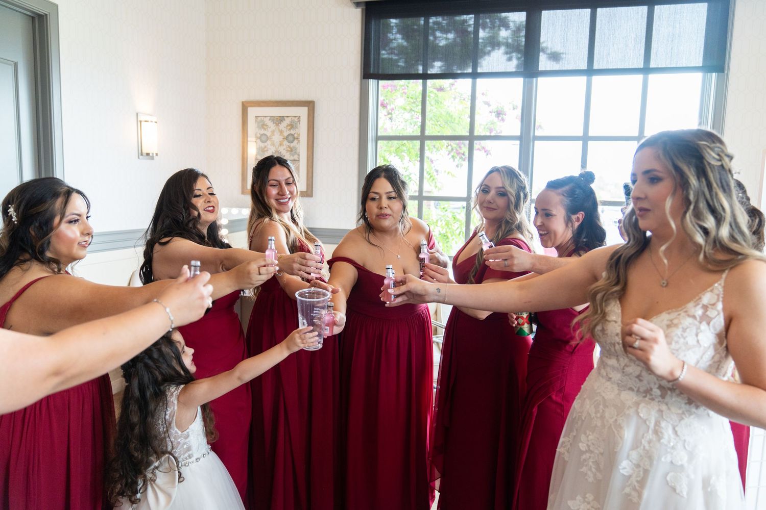 Wedding party members in red dresses share celebratory drinks together.