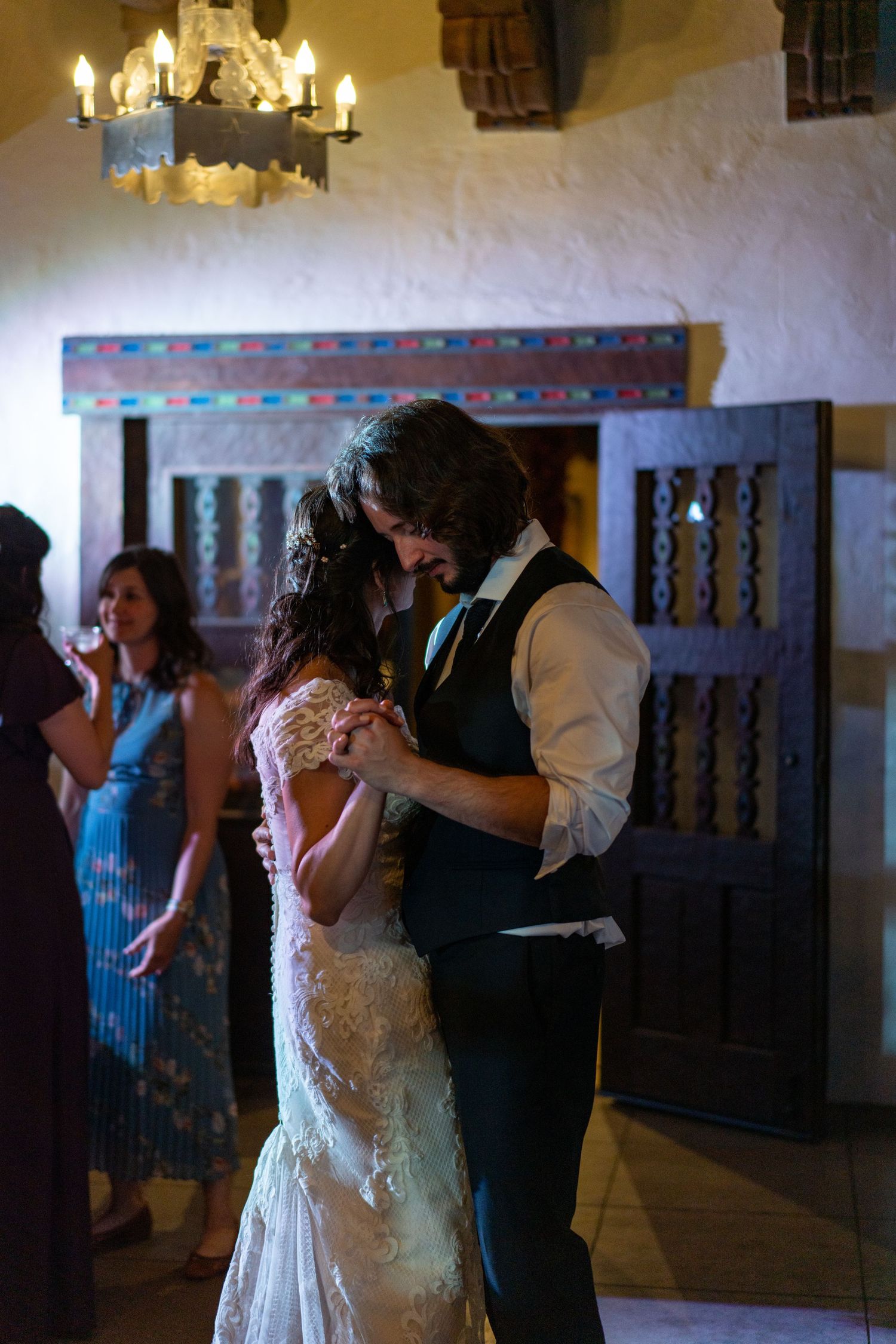 A couple dances intimately under a chandelier during their wedding reception.