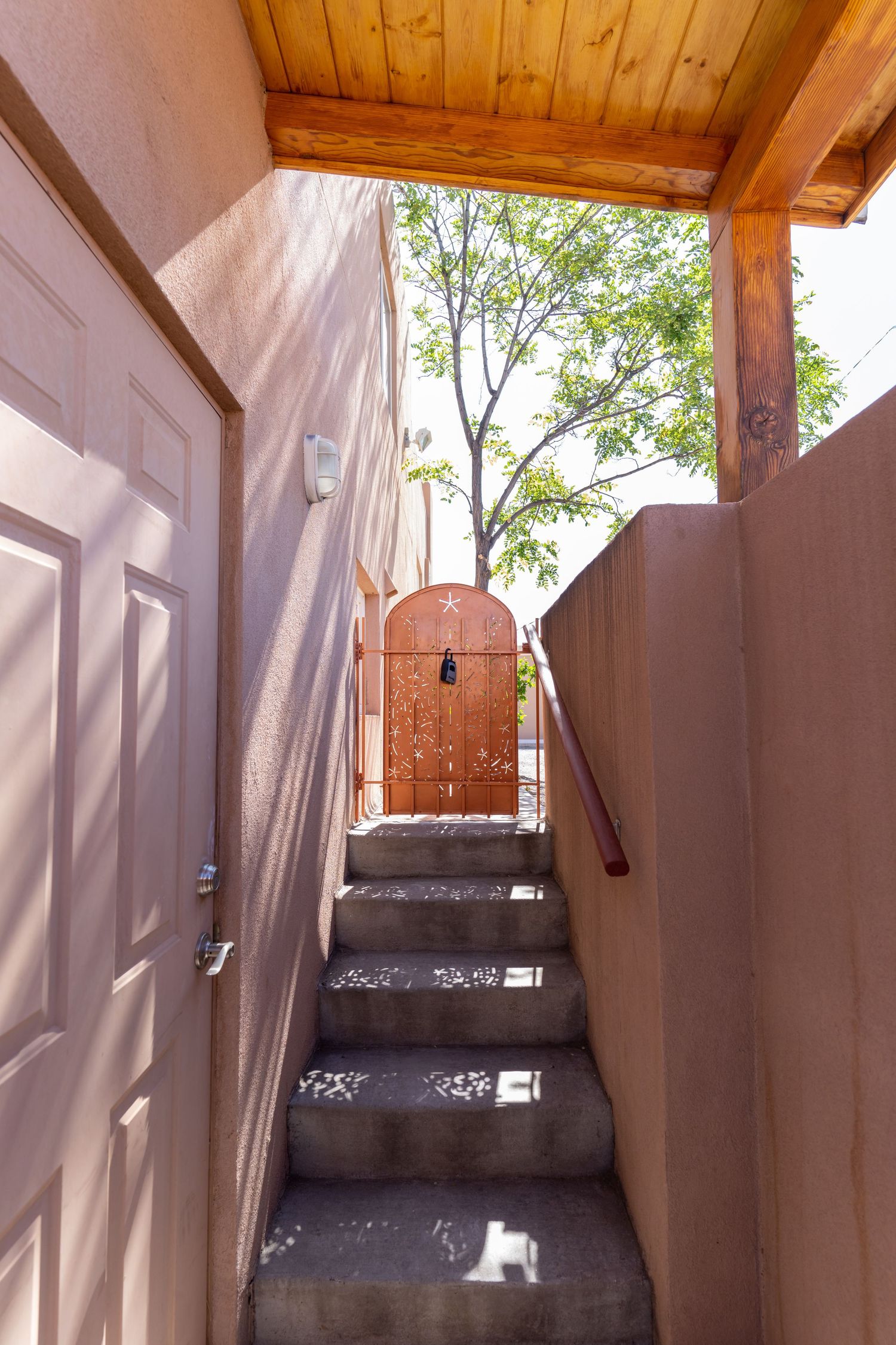 Outdoor walkway with adobe walls and wooden beams casting dramatic shadows in Southwestern architectural style.