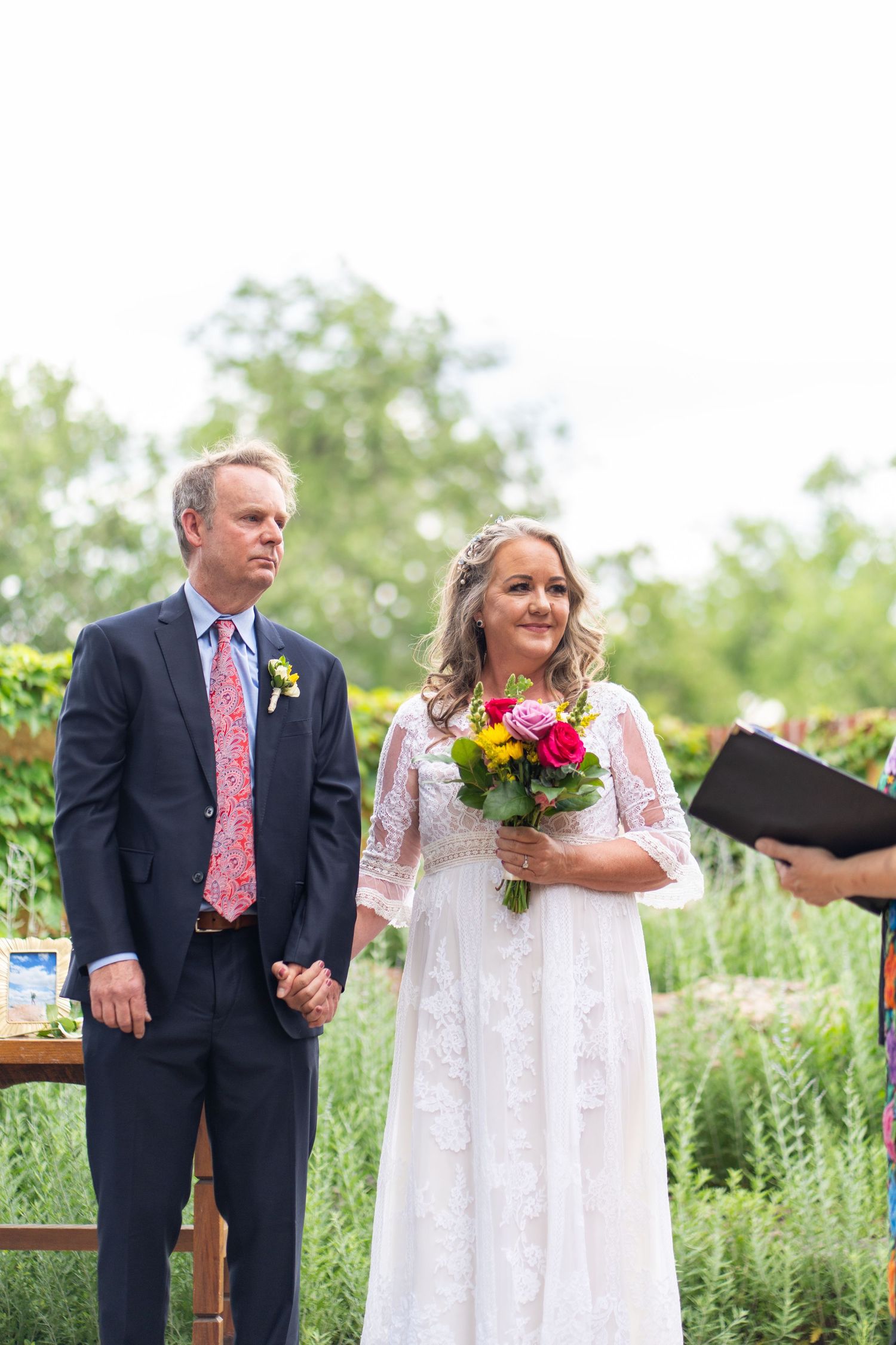 Outdoor wedding ceremony in a garden setting with lush greenery and colorful flowers.
