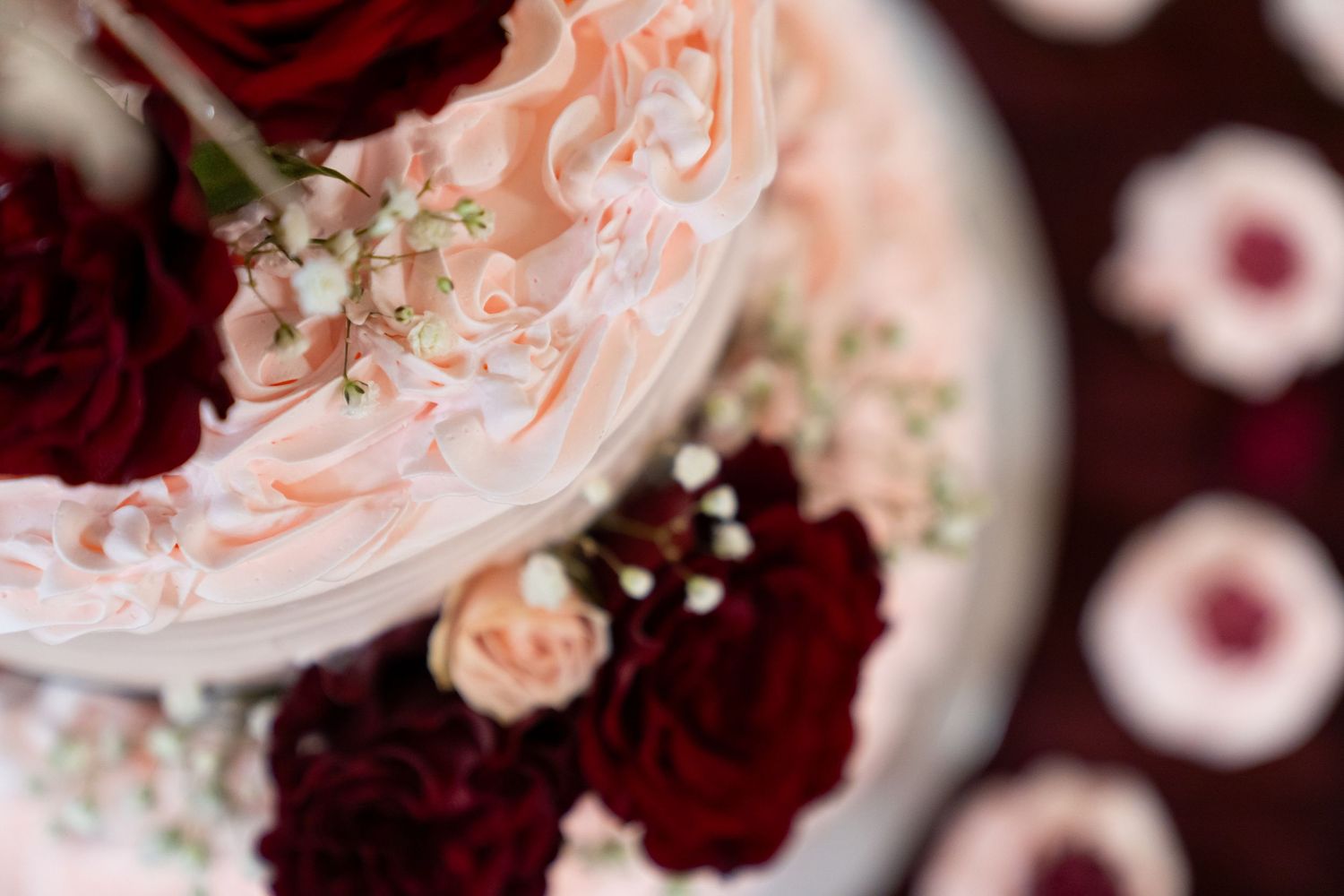Close-up detail of a wedding cake decorated with burgundy roses and blush pink flowers.