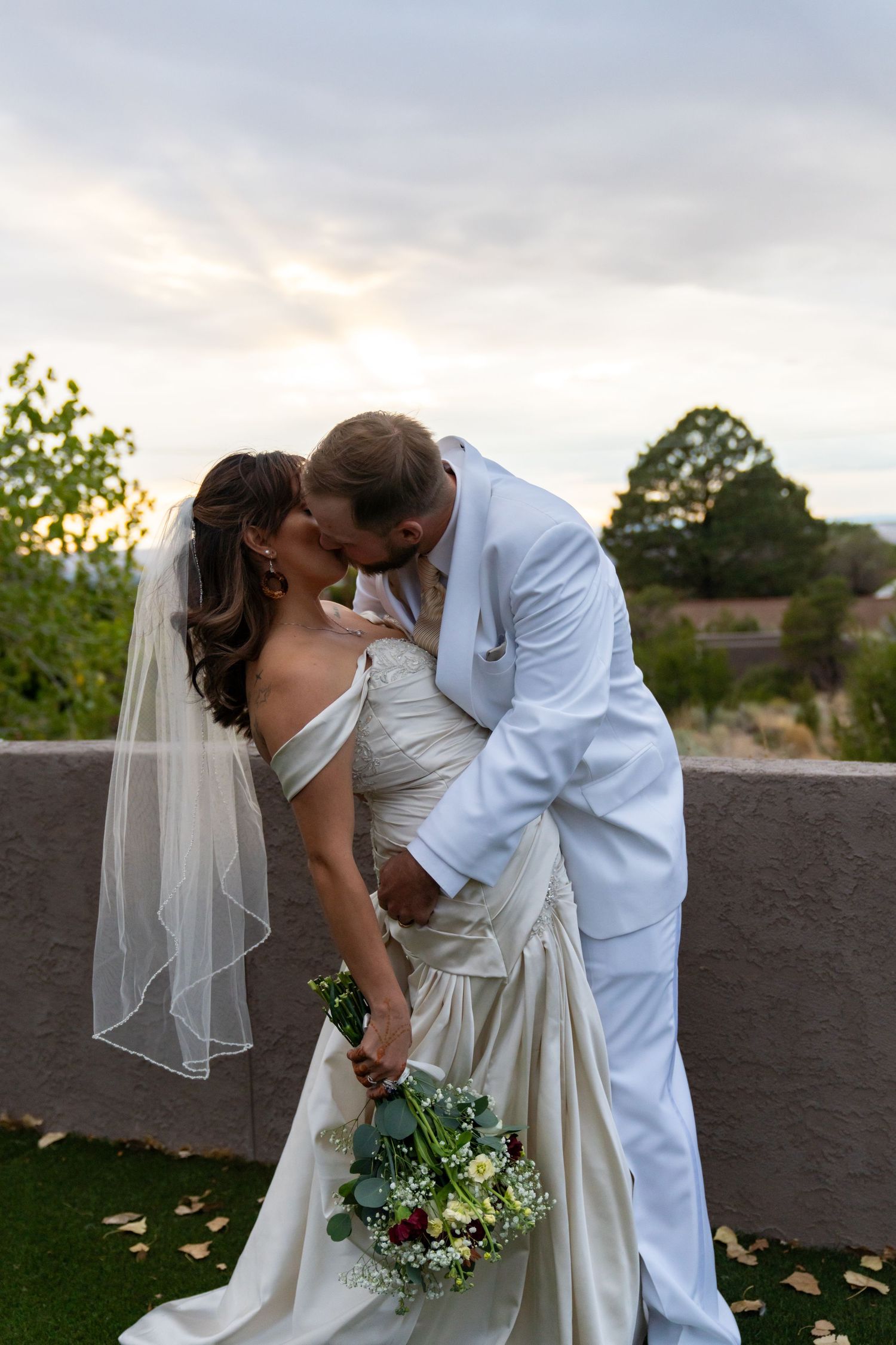 Romantic wedding couple sharing an intimate moment at sunset with the bride holding a white and green bouquet.