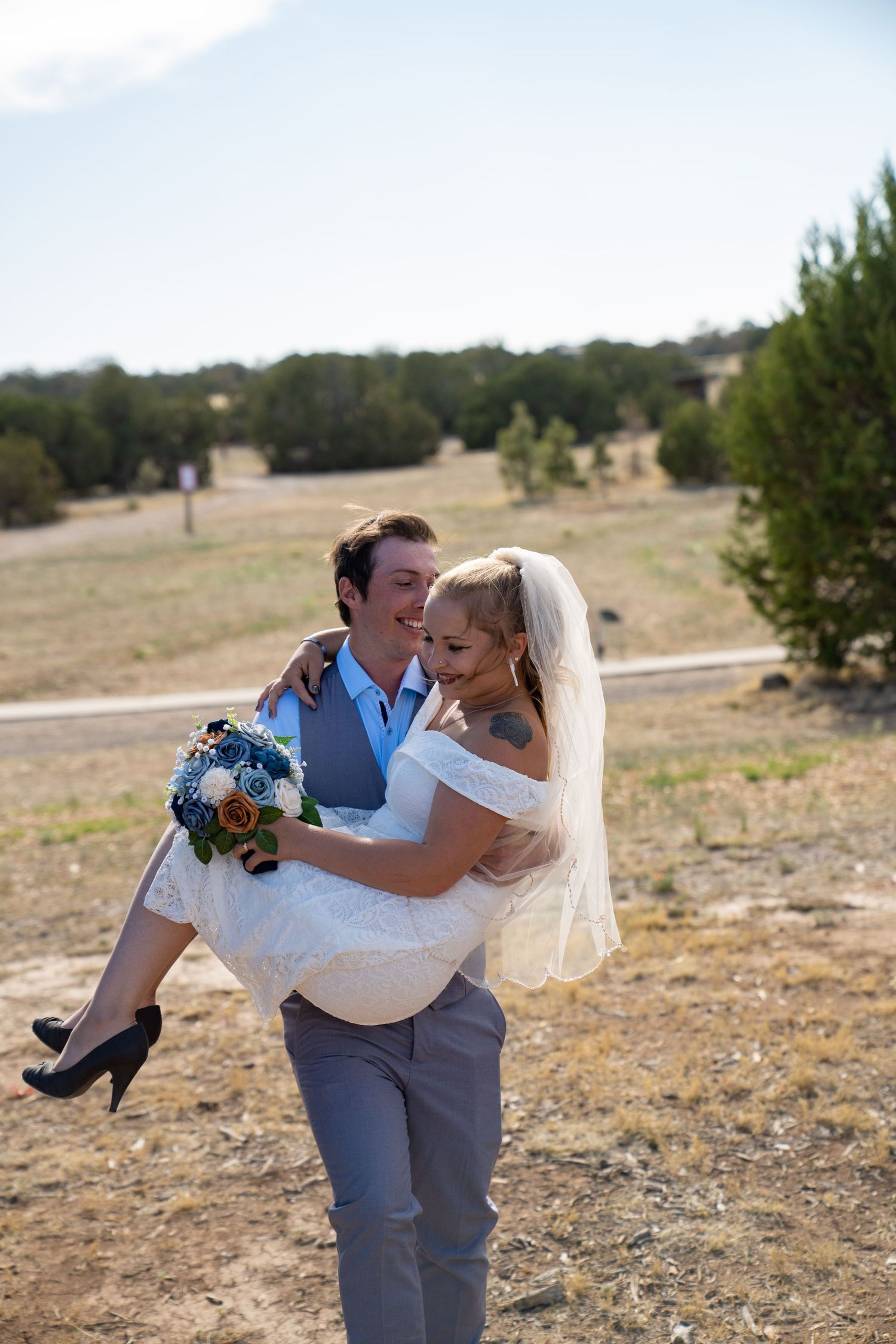 Couple embraces in romantic pose outdoors with natural landscape in background.