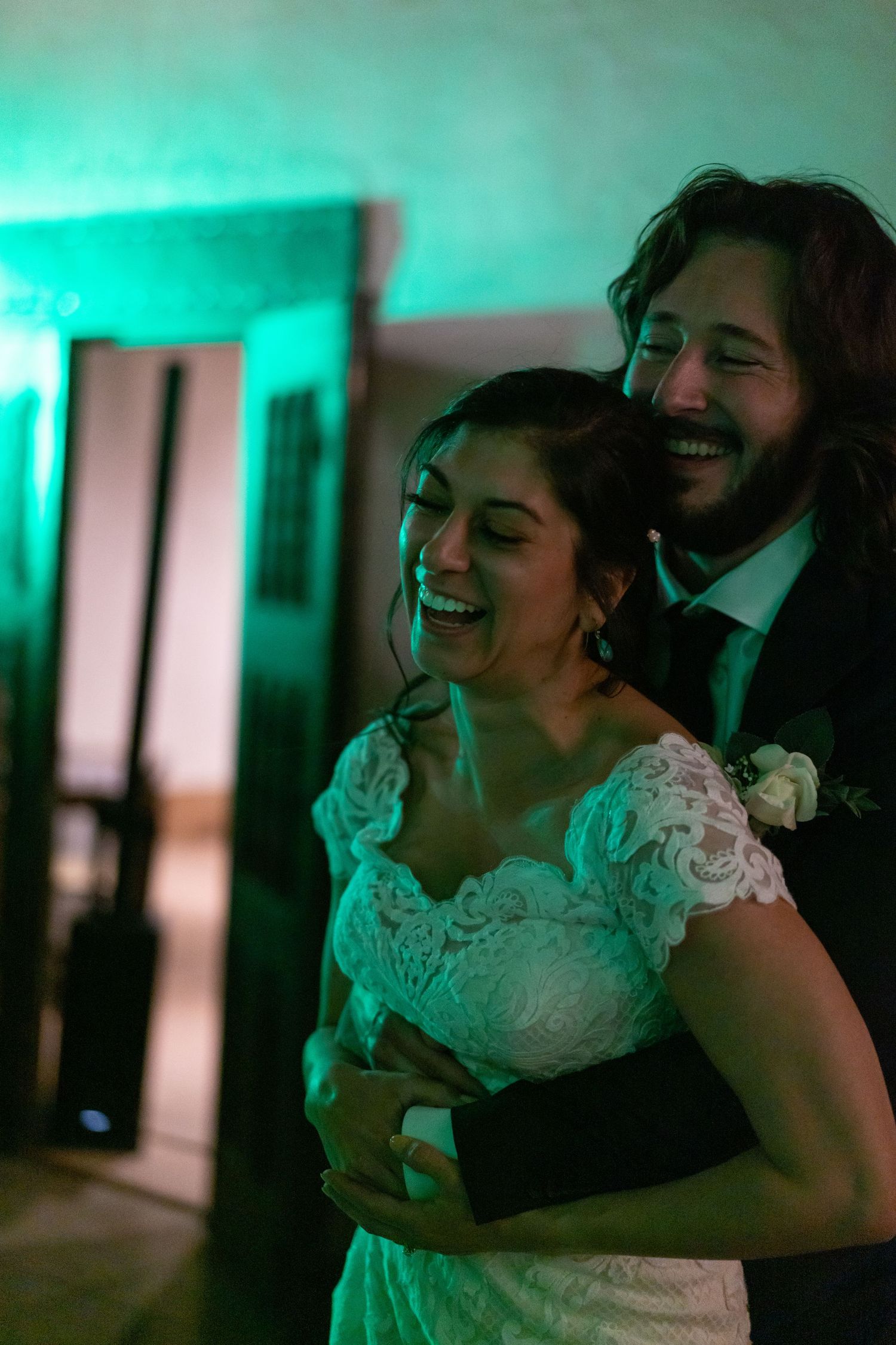 A couple shares a tender dance moment together under turquoise lighting at a wedding reception.