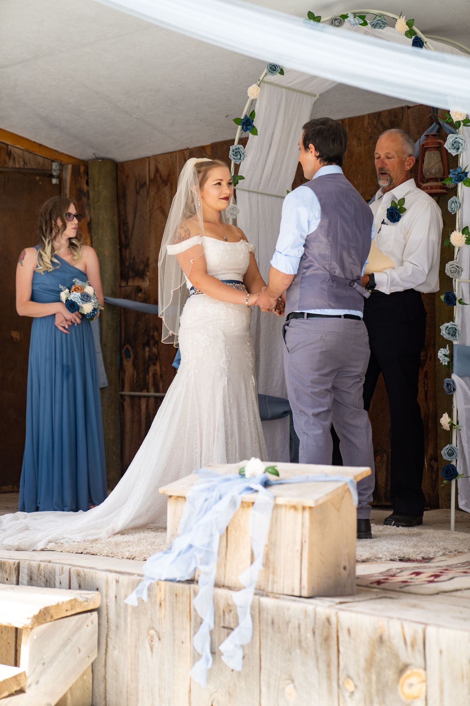 Wedding party members in blue bridesmaid dresses and gray suits gather on a covered porch during a celebration.