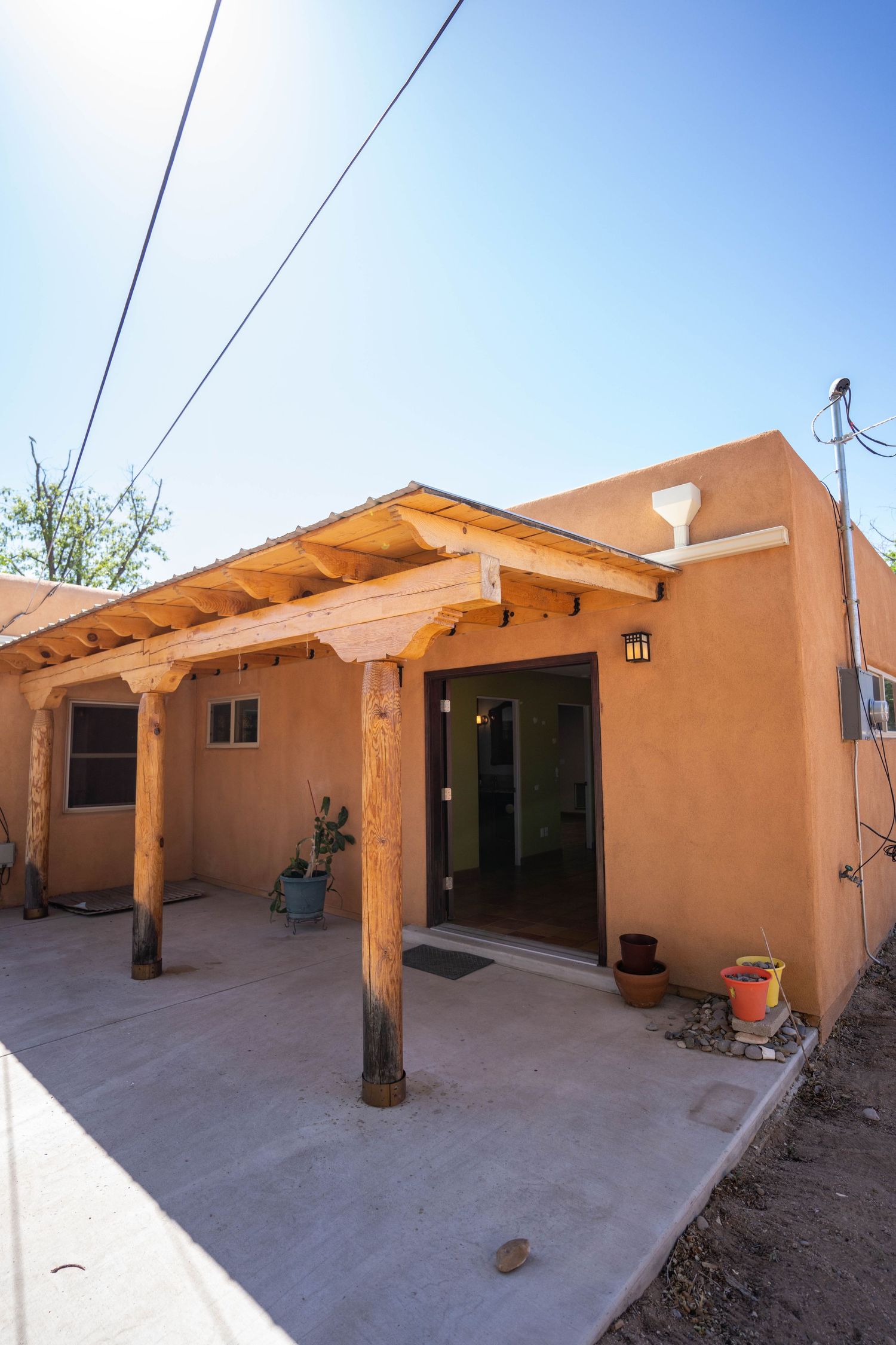 Adobe-style house exterior with wooden pergola and concrete patio showing multiple angles of the outdoor living space.