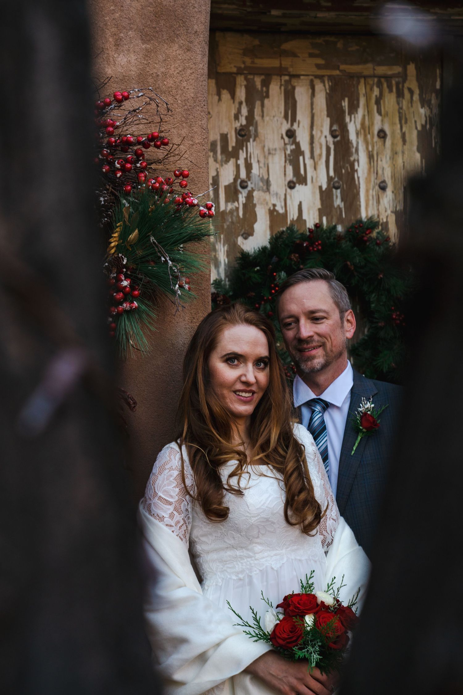 A winter wedding portrait with holiday decor featuring red berries and evergreen branches.