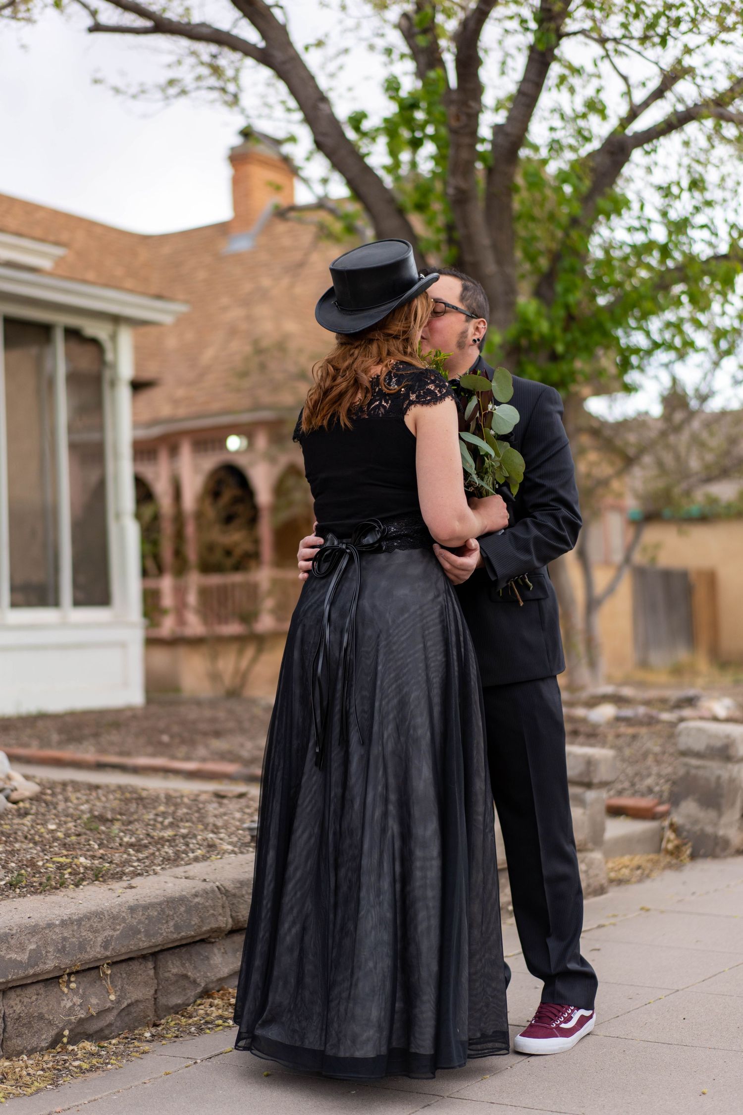 Two figures in black attire share an intimate moment while sitting on outdoor steps.