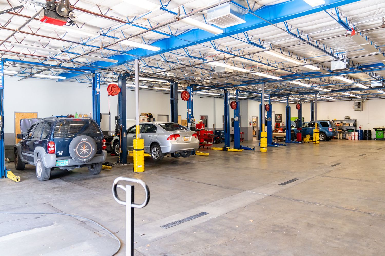Large commercial auto repair garage interior with multiple vehicle lifts and bright blue overhead lighting fixtures.