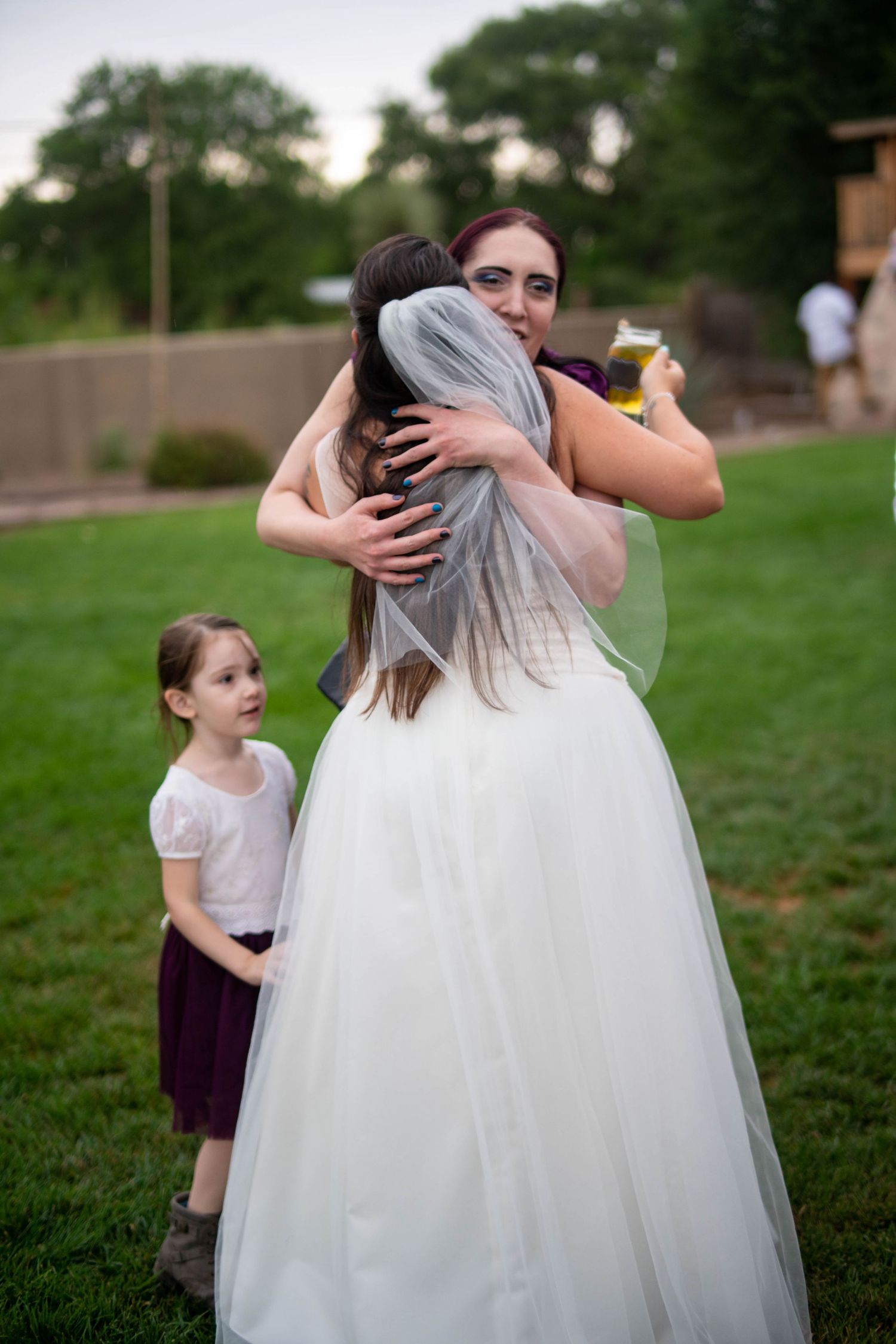 Wedding guests embrace and interact on a grassy lawn during an outdoor reception.