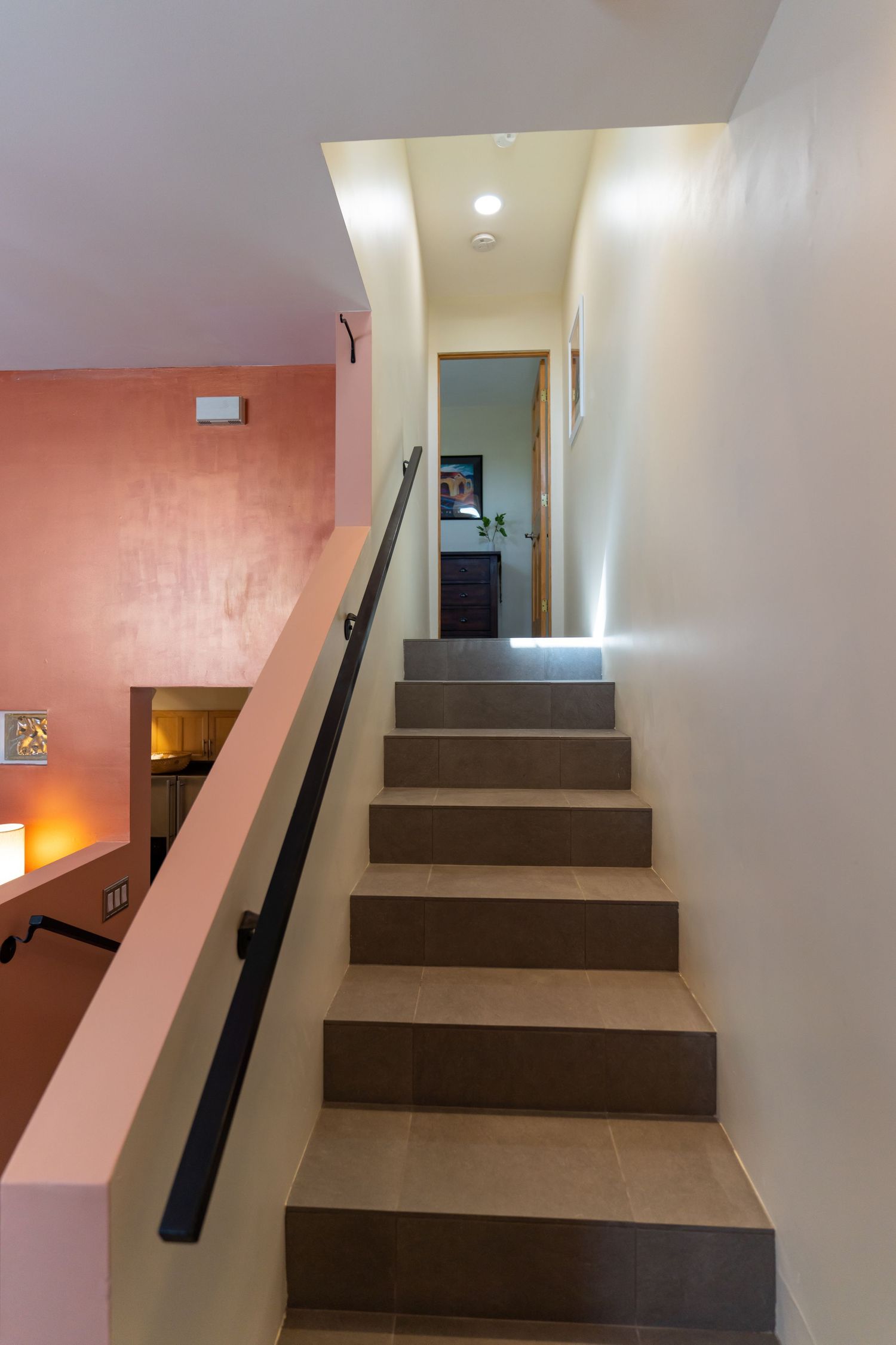 Modern interior staircase with brown steps and black handrail against white walls and pink accent wall in background.
