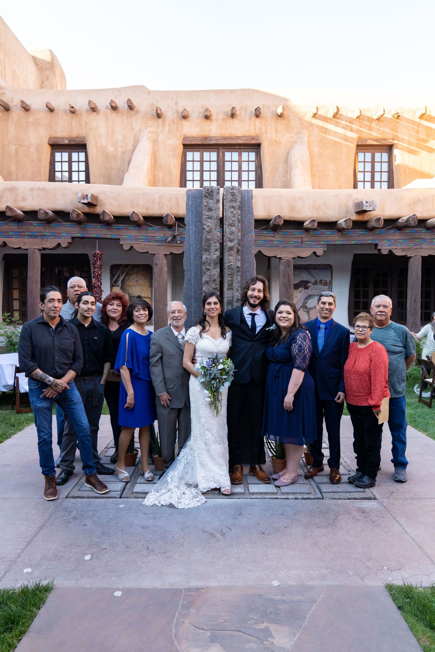 Wedding party poses in front of adobe-style building with wooden beams and rustic architecture.