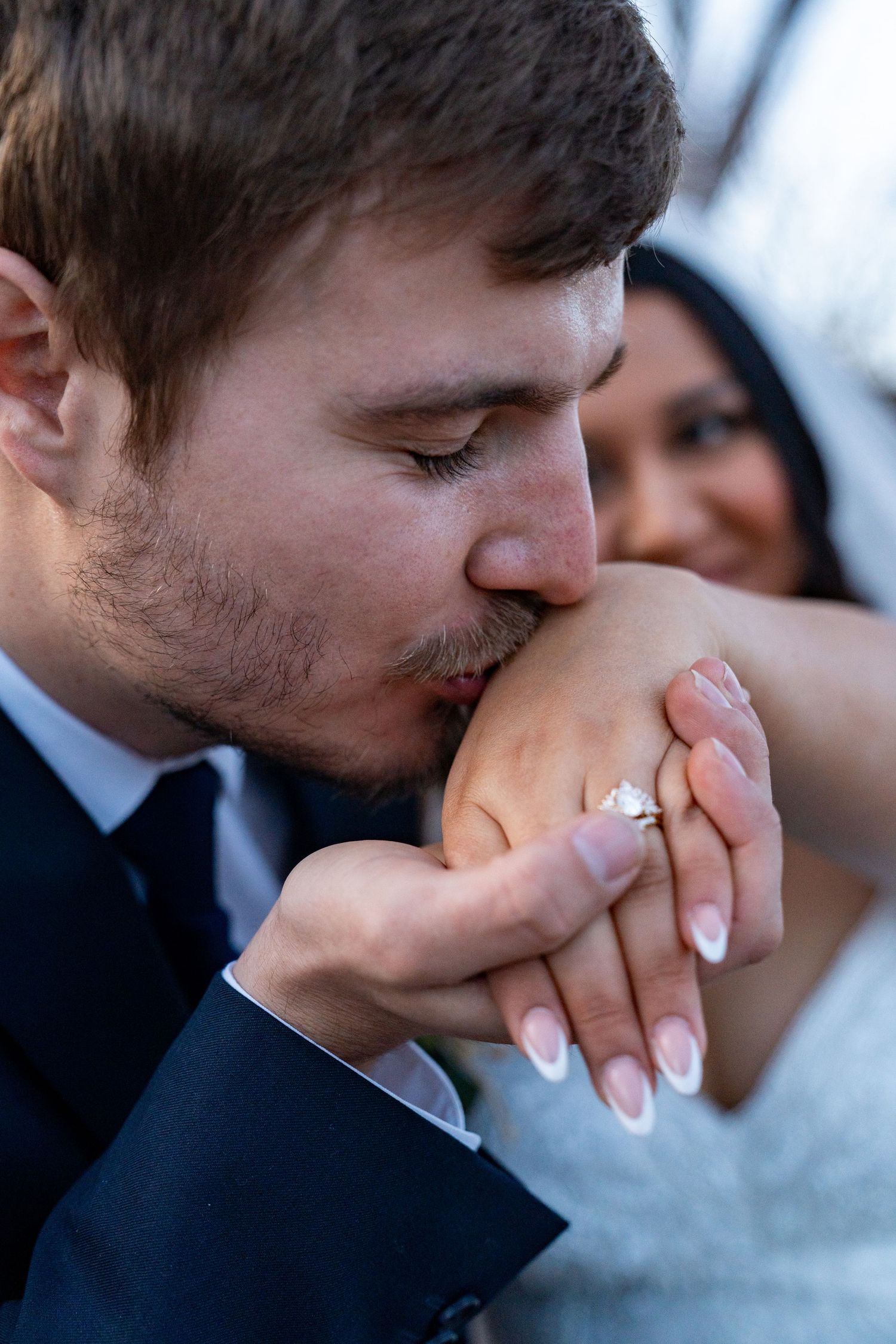 A tender moment as a groom kisses his bride's hand, showcasing her engagement ring.