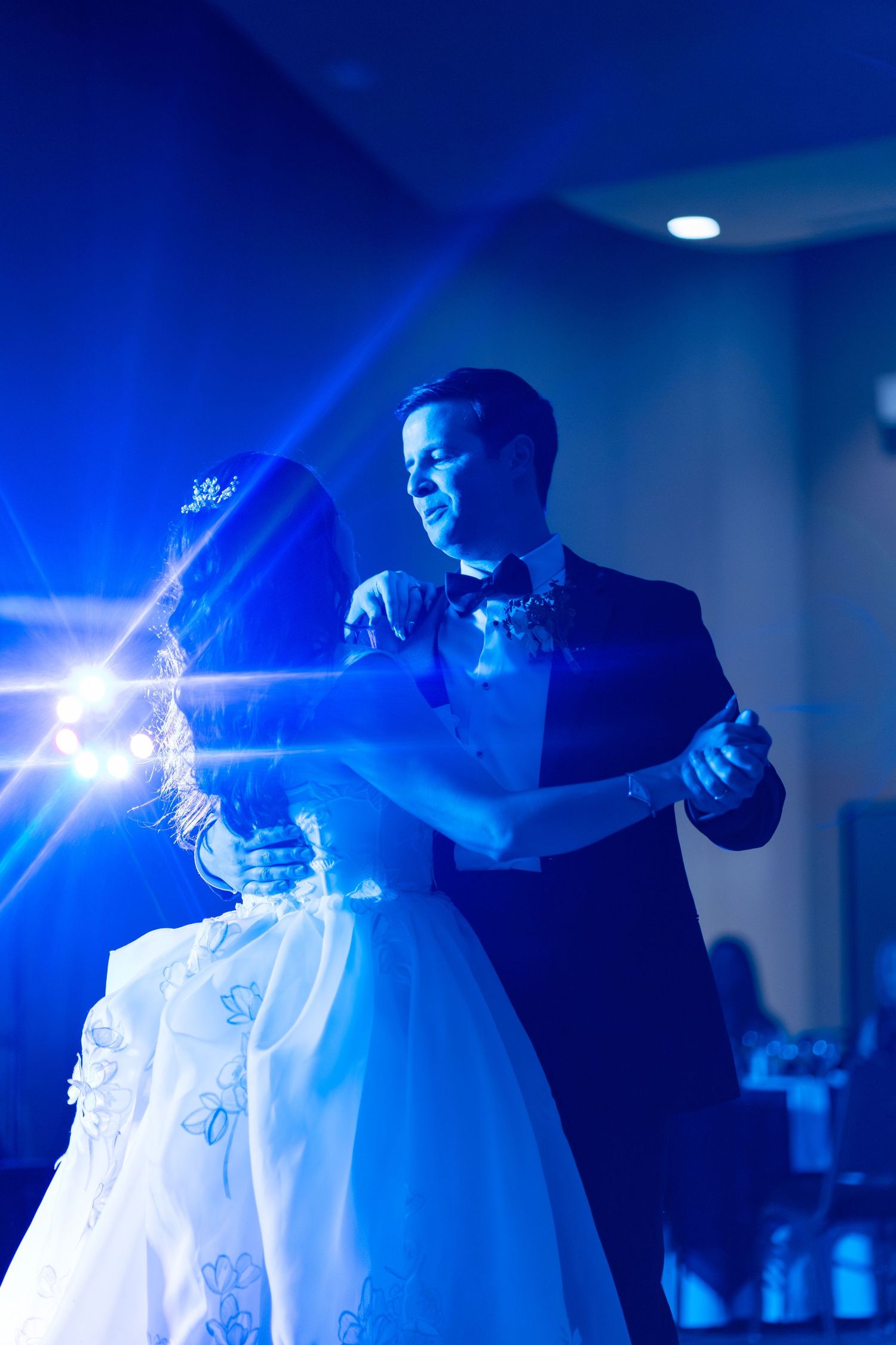 Bride and groom share their first dance bathed in blue lighting at their wedding reception.