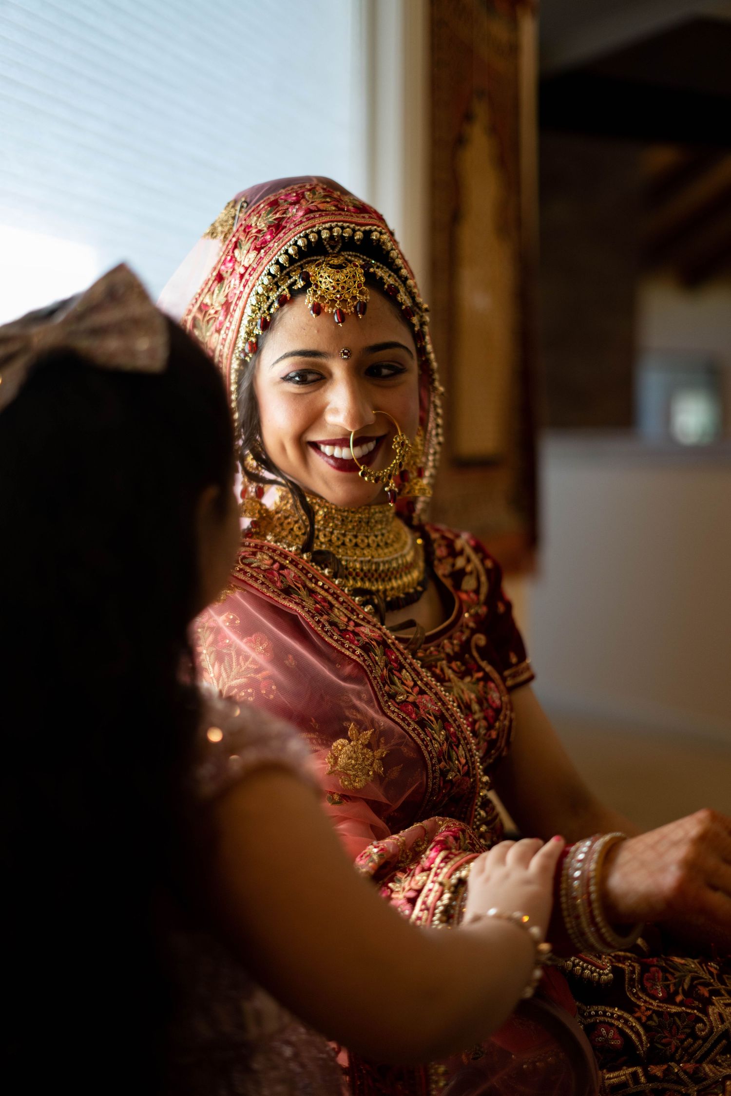 Traditional Indian bride in red and gold attire with ornate jewelry and decorative accessories in warm lighting.