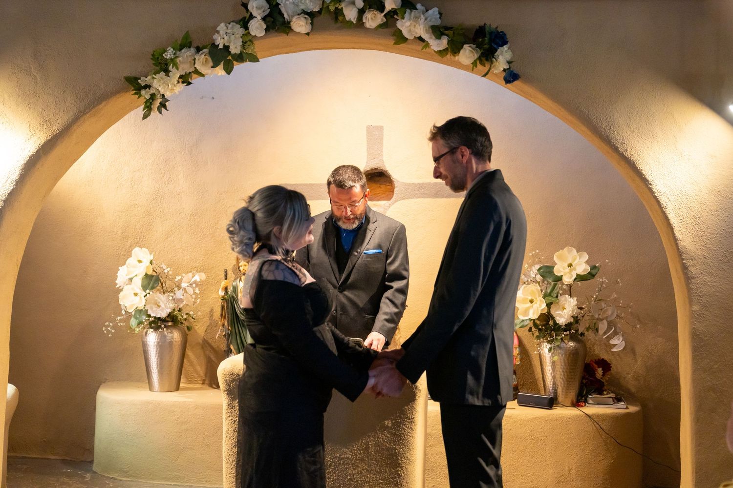 An intimate wedding ceremony moment under an elegant arched doorway with floral decorations.