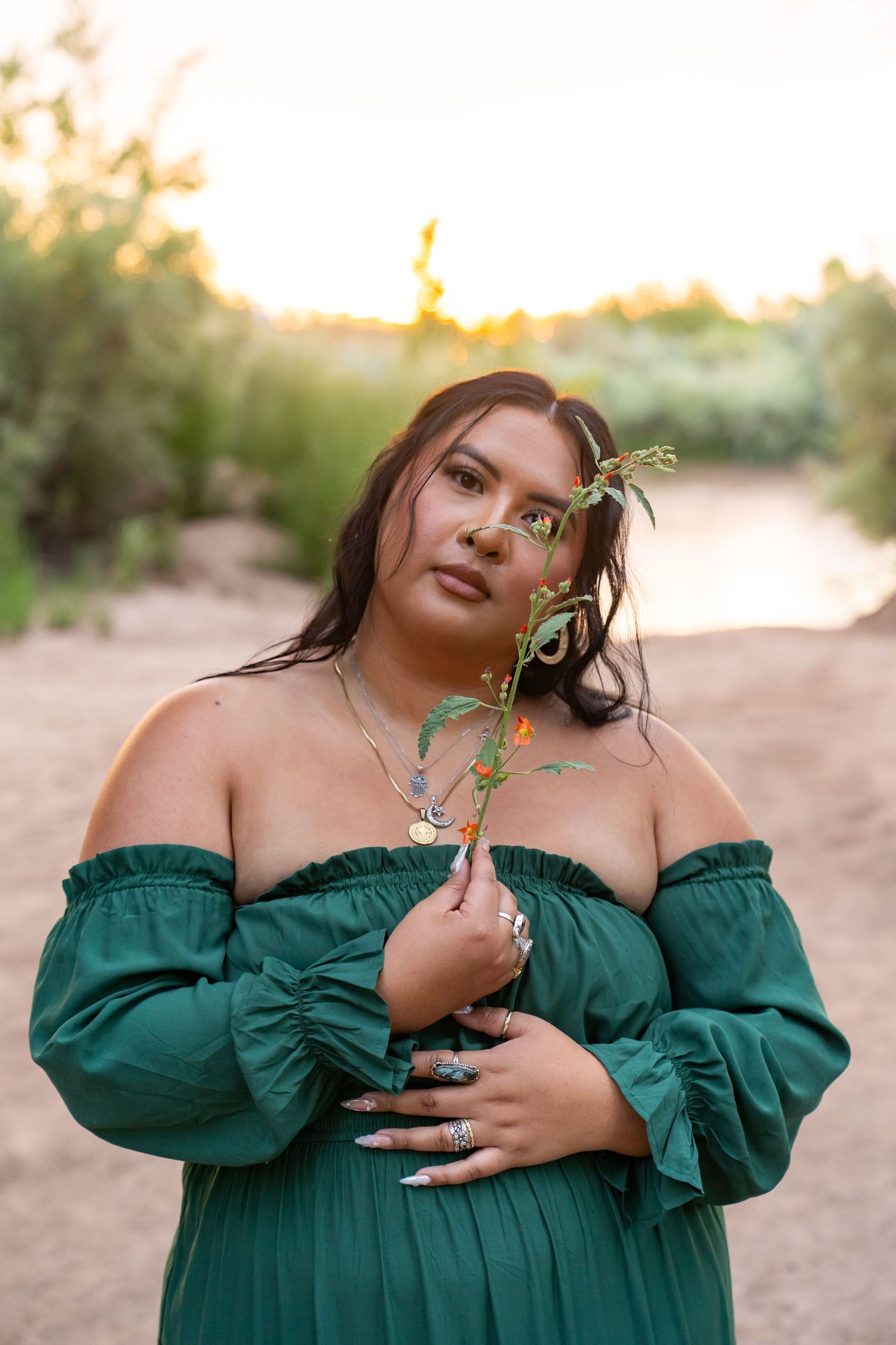 Portrait in green off-shoulder dress holding delicate plant stem at golden hour.