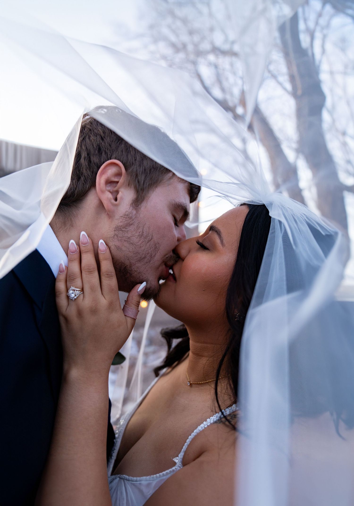 A tender wedding kiss moment captured through a flowing white veil.