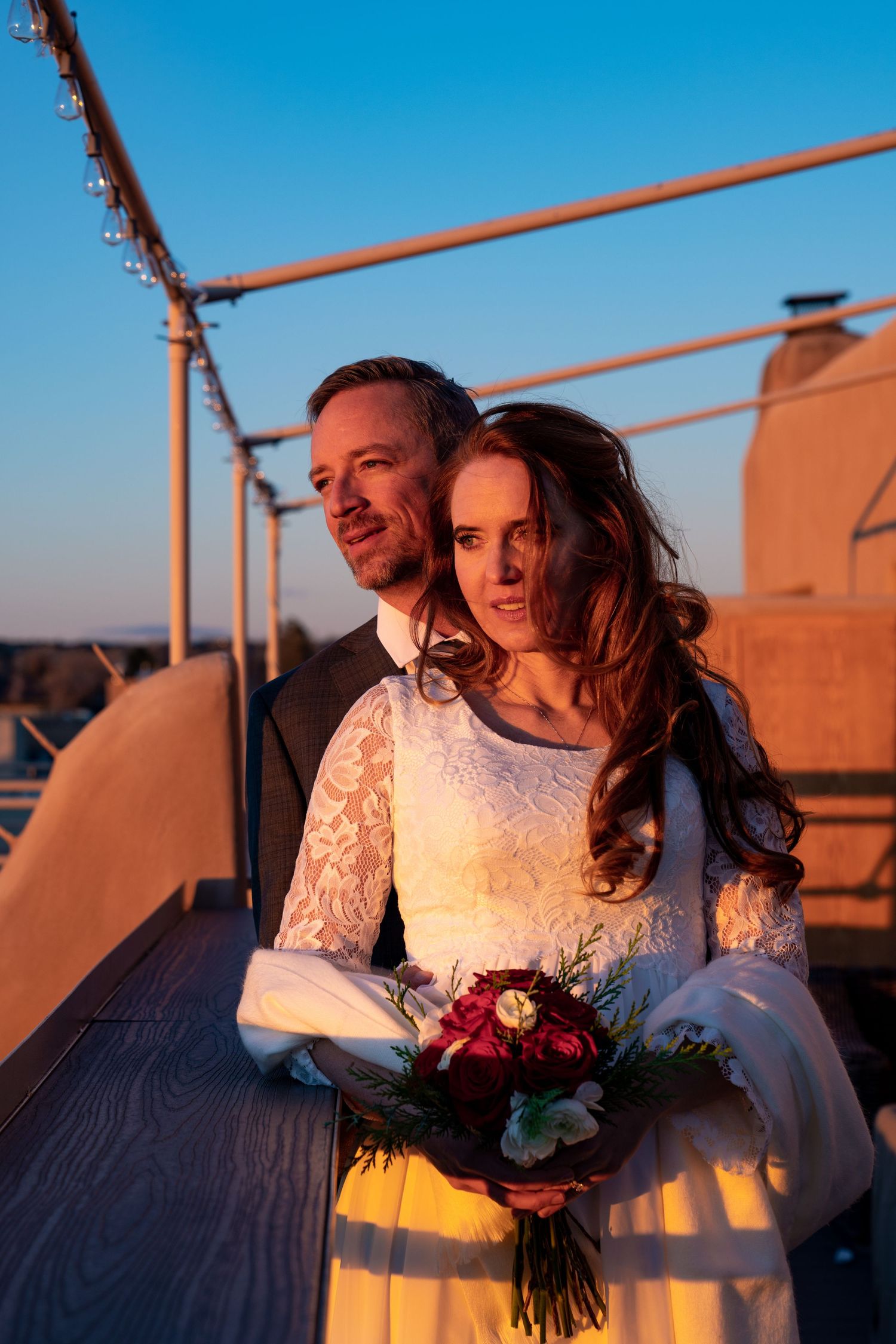 A sunset wedding portrait on a rooftop with warm golden light and a red bouquet.