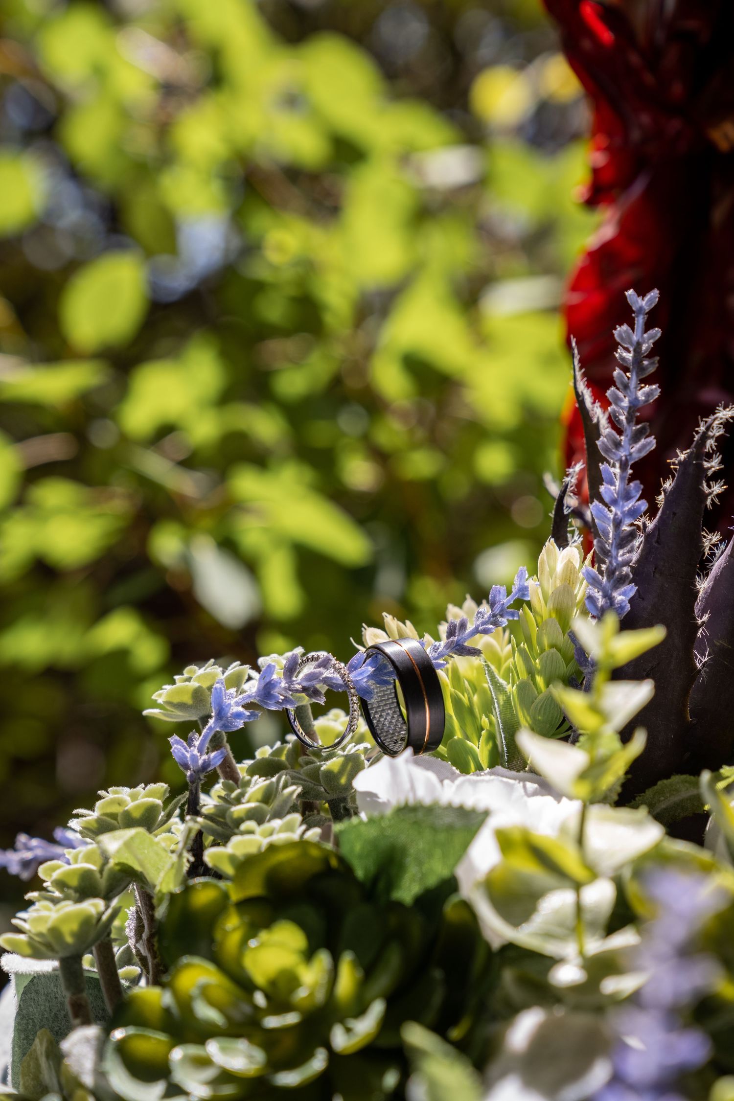 Wedding rings nestled among delicate purple flowers and greenery in a bridal bouquet.