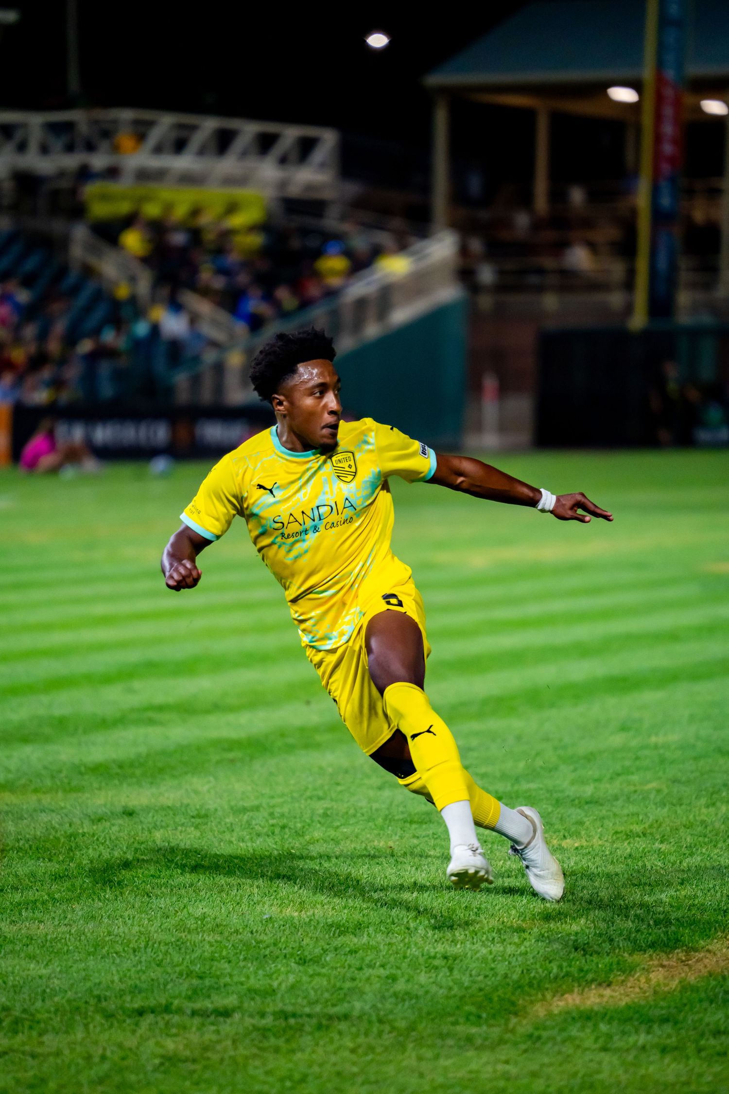 Soccer player in yellow Puma kit dribbles on green field during night match.