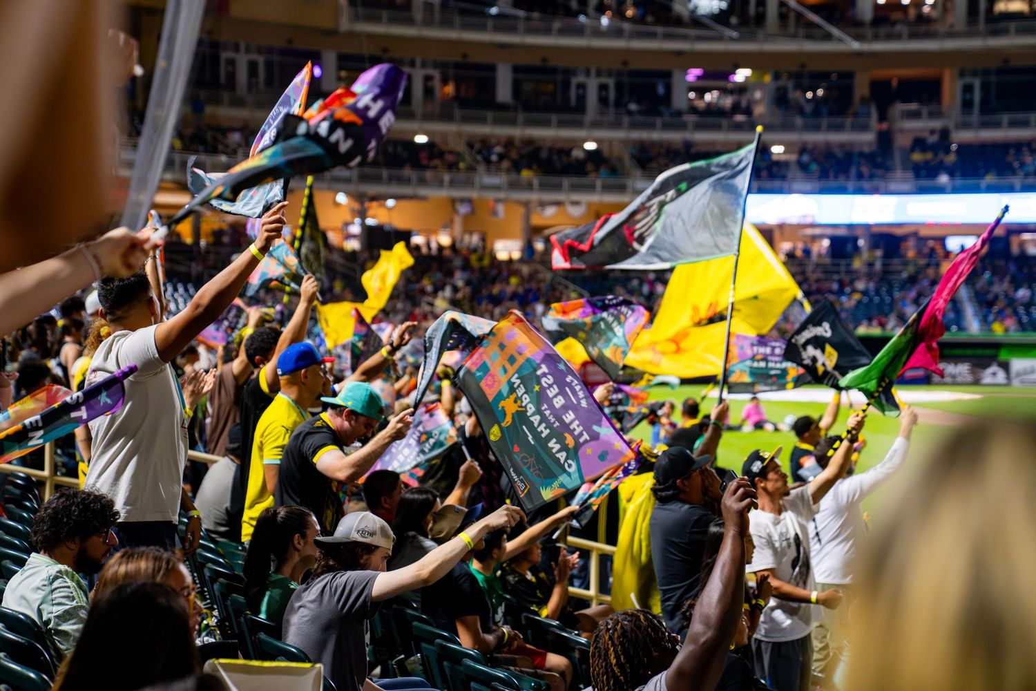 Excited sports fans wave colorful flags in packed stadium stands during a lively nighttime event.