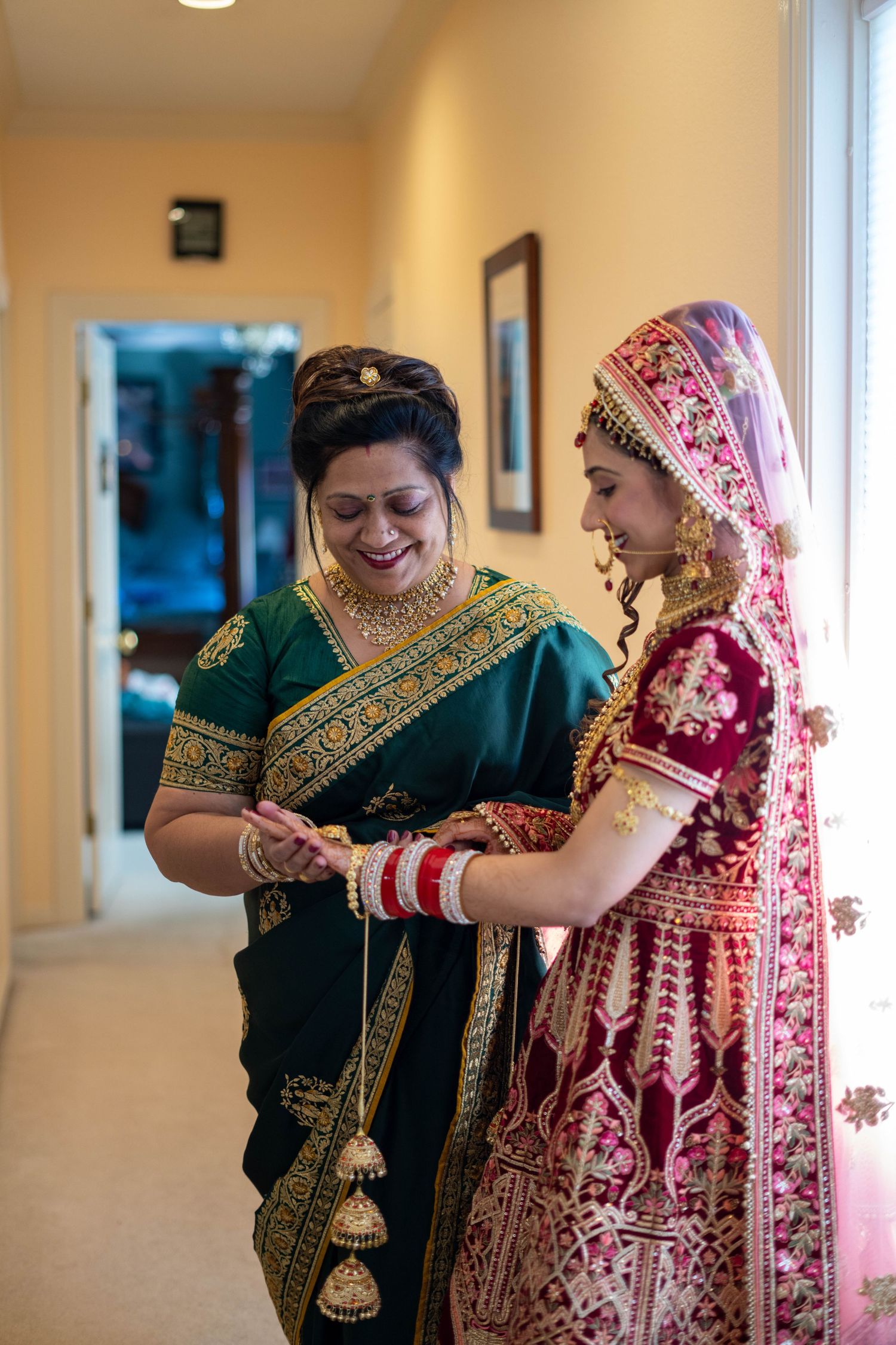 Women in traditional Indian outfits gather indoors for pre-wedding rituals wearing emerald and burgundy ethnic wear.