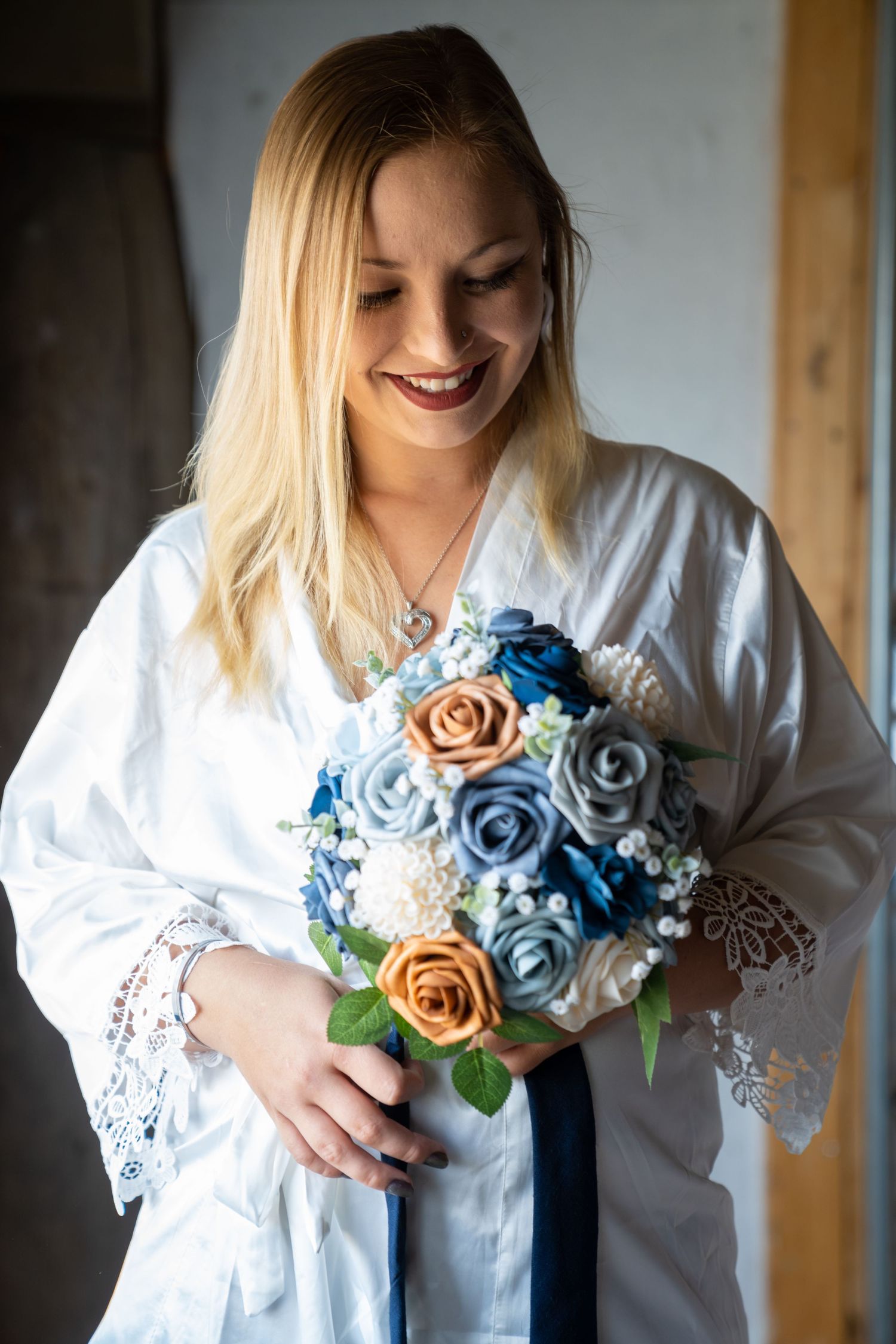 A person in a white lace blouse holds handmade blue and peach fabric roses against a dark background.