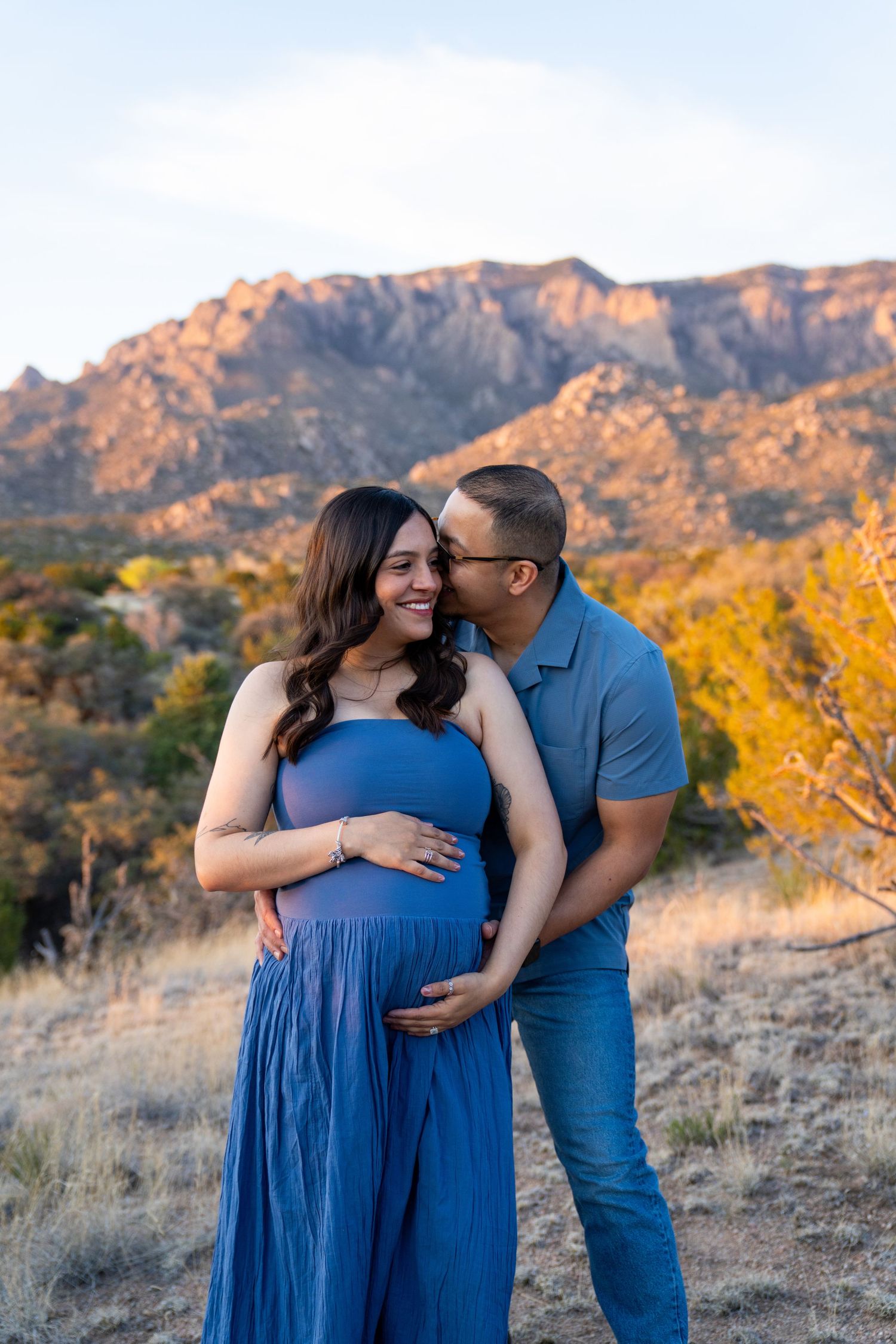 A couple poses outdoors during a maternity shoot, with mountains and golden foliage in the background.